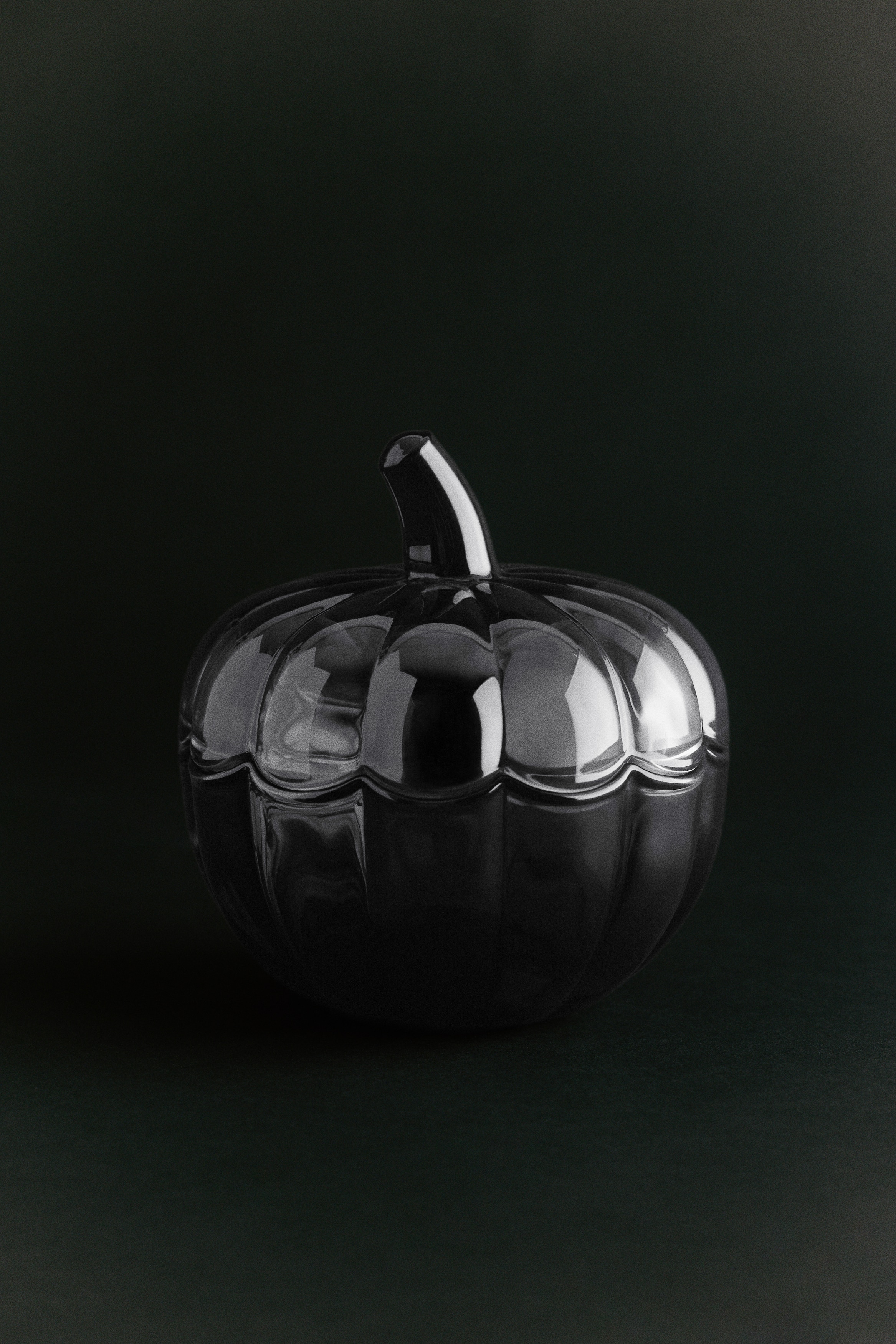 A dark grey translucent glass jar with a lid is forming a pumpkin shape. It is featuring ribbed sides and a stem on its lid.