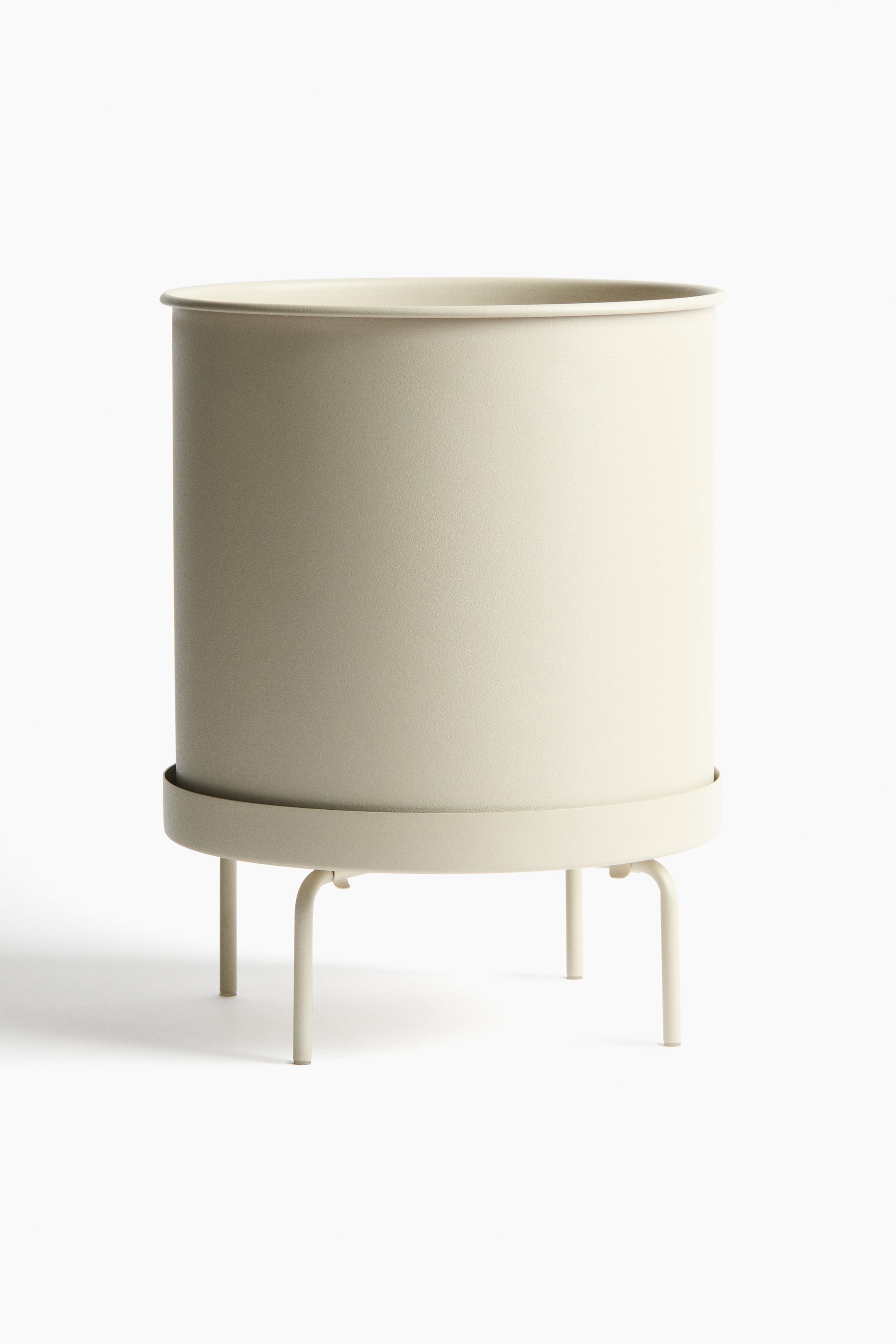 View larger image: An extra-large, cylindrical metal plant pot, in a light neutral colour, is sitting on a matching metal plant stand, facing front. The stand features a circular saucer supporting the pot and four curved legs.