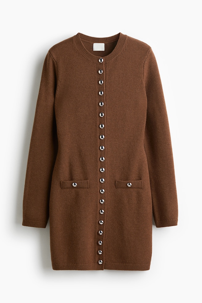 Un lungo cardigan marrone viene mostrato dalla parte anteriore, caratterizzato da uno scollo rotondo a coste e maniche lunghe. È progettato con un'abbottonatura completa di diciannove bottoni color argento e due tasche applicate vicino all'orlo, ciascuna fissata con un bottone abbinato color argento. - 1