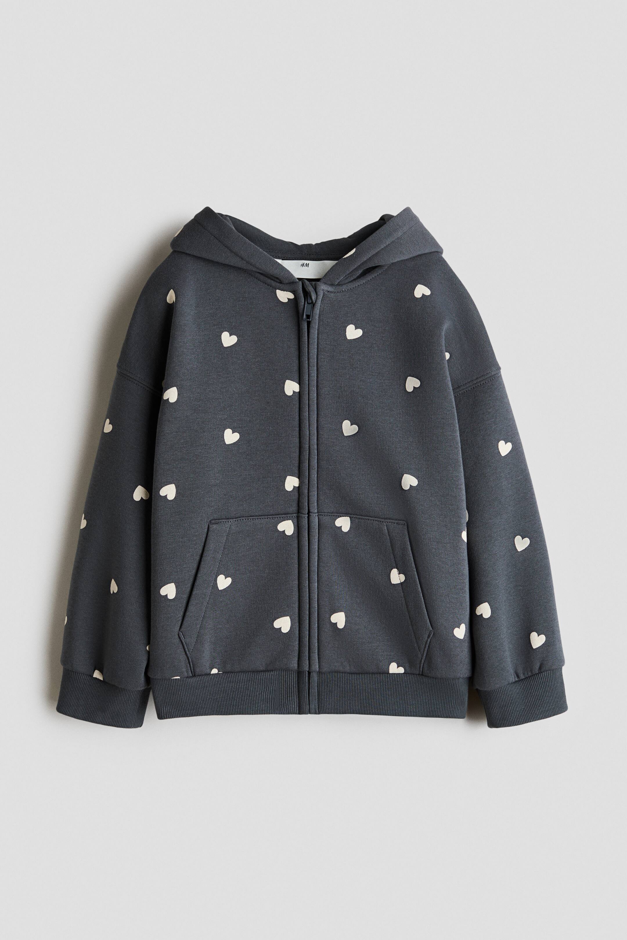View larger image: A dark grey zip-up hoodie showcases an all-over pattern of small, light-coloured hearts. It features a hood, a full-length front zipper, a kangaroo pocket, and ribbed cuffs and hem.