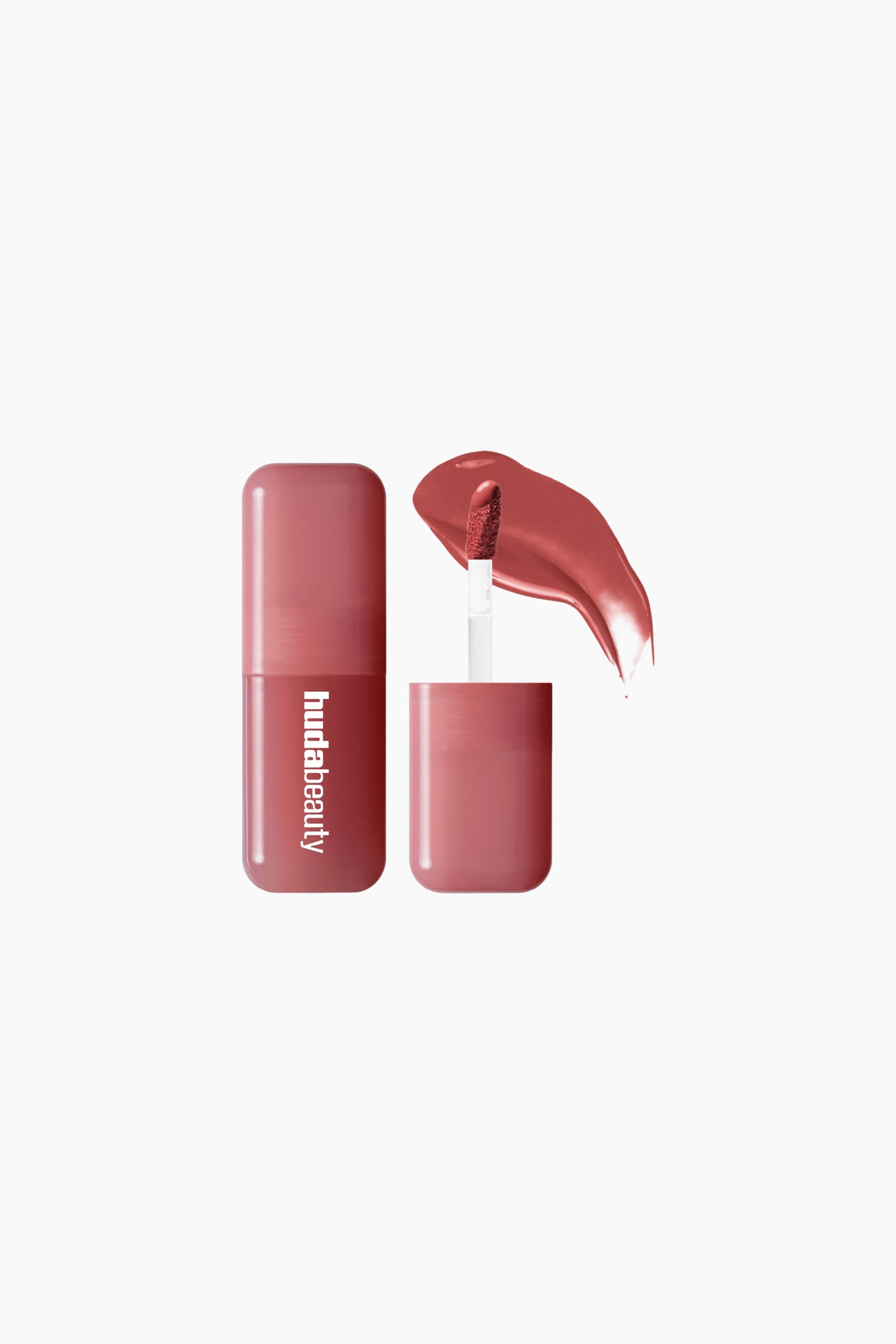 Vis større bilde: En støvete rose Huda Beauty leppeproduktbeholder står oppreist og viser merkevarenavnet vertikalt. Lokket er fjernet, og en applikator med dåefot, dekket med det flytende produktet, stikker ut fra lokket, med en glansfull prøve av produktet som vises til høyre.
