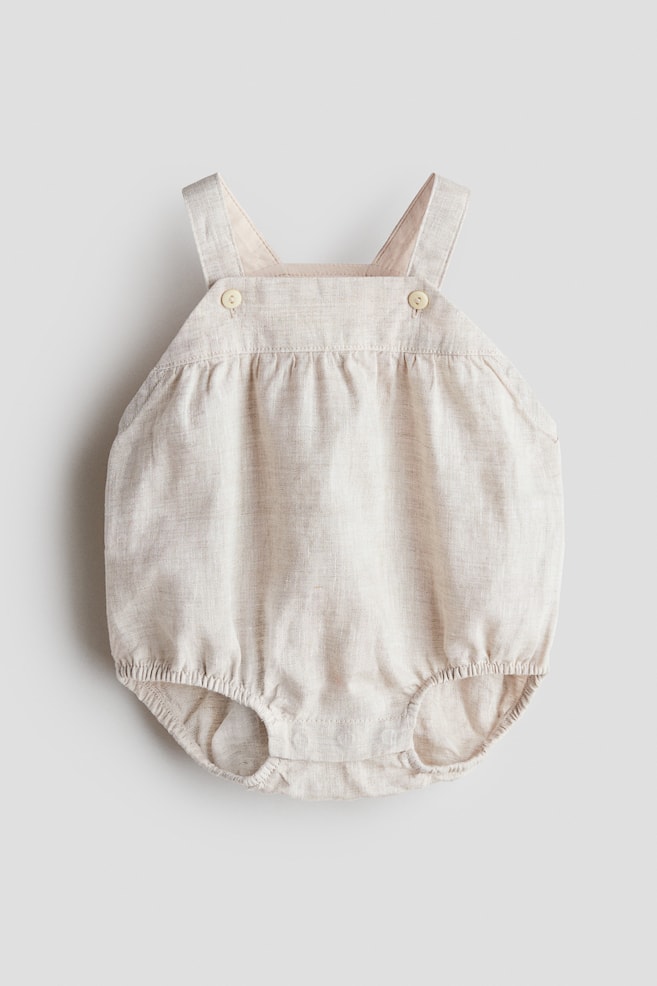 A beige linen bubble romper is displaying its front, featuring two shoulder straps attached with light-colored buttons and elasticized leg openings. - 1