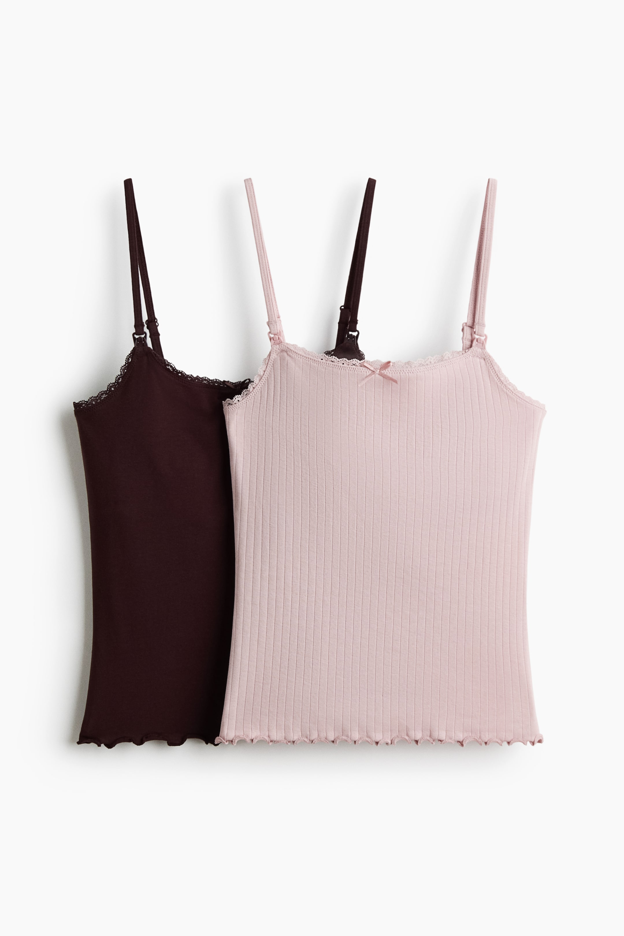View larger image: Two short, fitted nursing tops, one in a light pink shade and the other in a deep brown hue, are showcased at the front. Both tops boast a ribbed jersey texture, lace-trimmed necklines, and slender shoulder straps equipped with practical nursing clasps. A delicate satin bow embellishes the front of the pink top, while both pieces are finished with an overlocked hem.