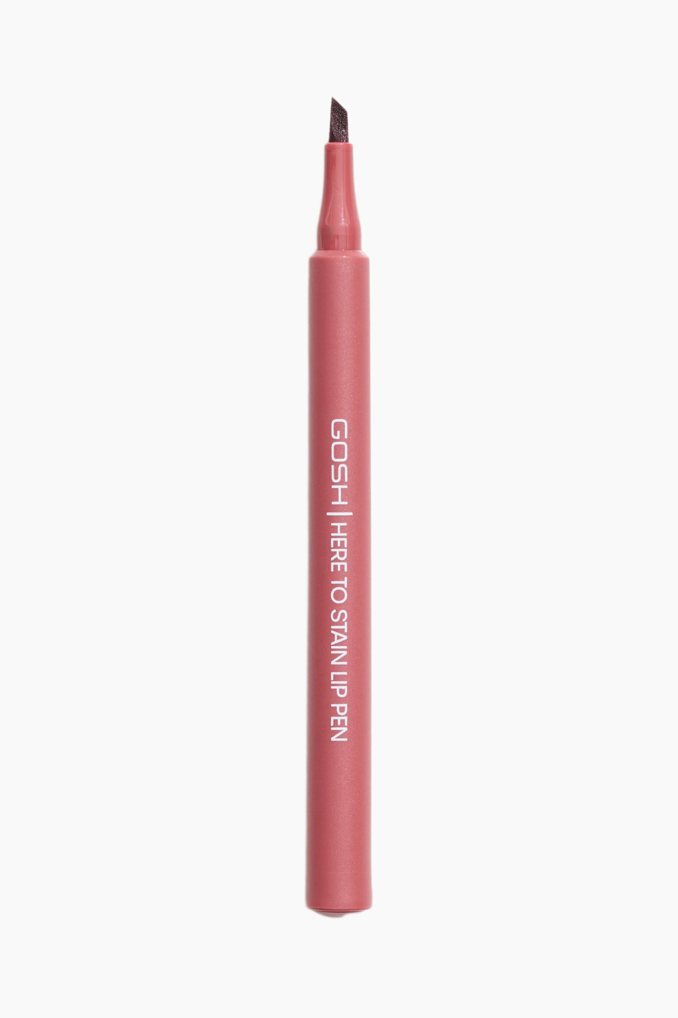 Se større billede: En GOSH Here to Stain Lip Pen står oprejst og vender fremad, med en støvet rosa cylindrisk krop og en mørkebrun vinklet filtspids. Produktnavnet "GOSH | HERE TO STAIN LIP PEN" er trykt vertikalt på siden.