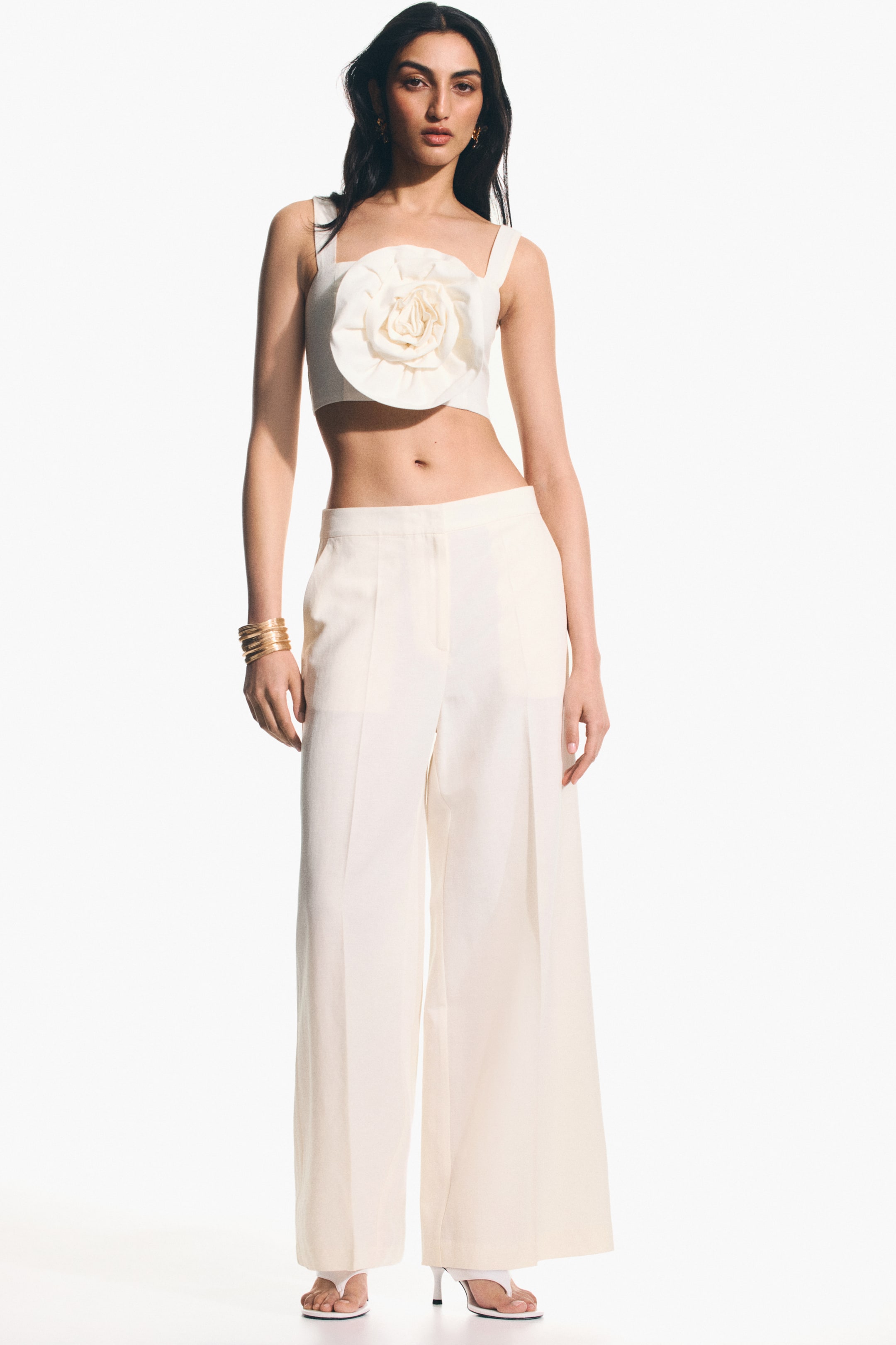 View larger image: The model is wearing ankle-length, high-waisted trousers with an airy weave. These trousers showcase a flat front, diagonal side pockets, and wide legs with creases down the front.