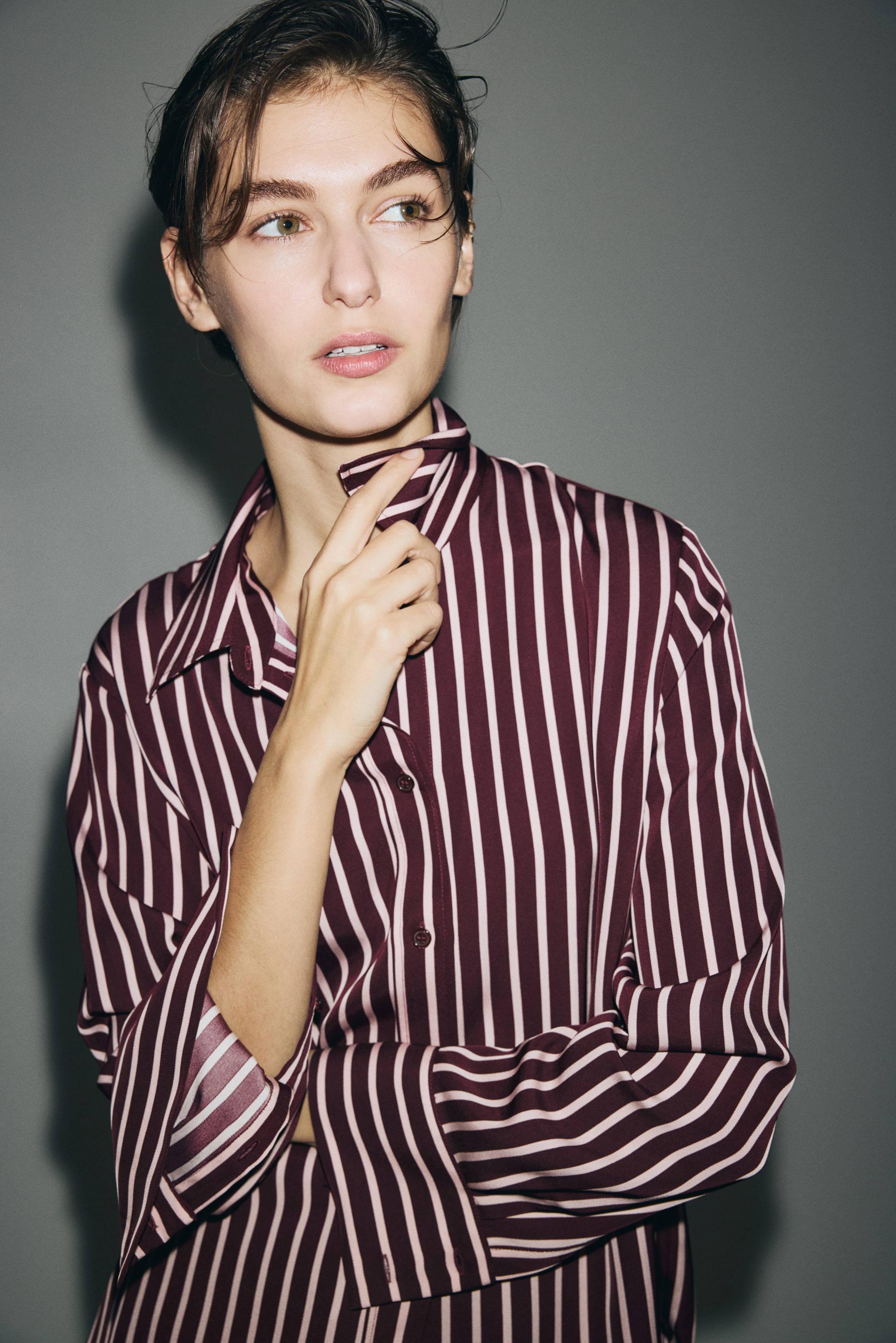 Voir une image plus grande: Une chemise ample à boutons sur le devant présente des rayures verticales bordeaux et rose pâle. Elle a un col pointu et ses manches longues sont retroussées.