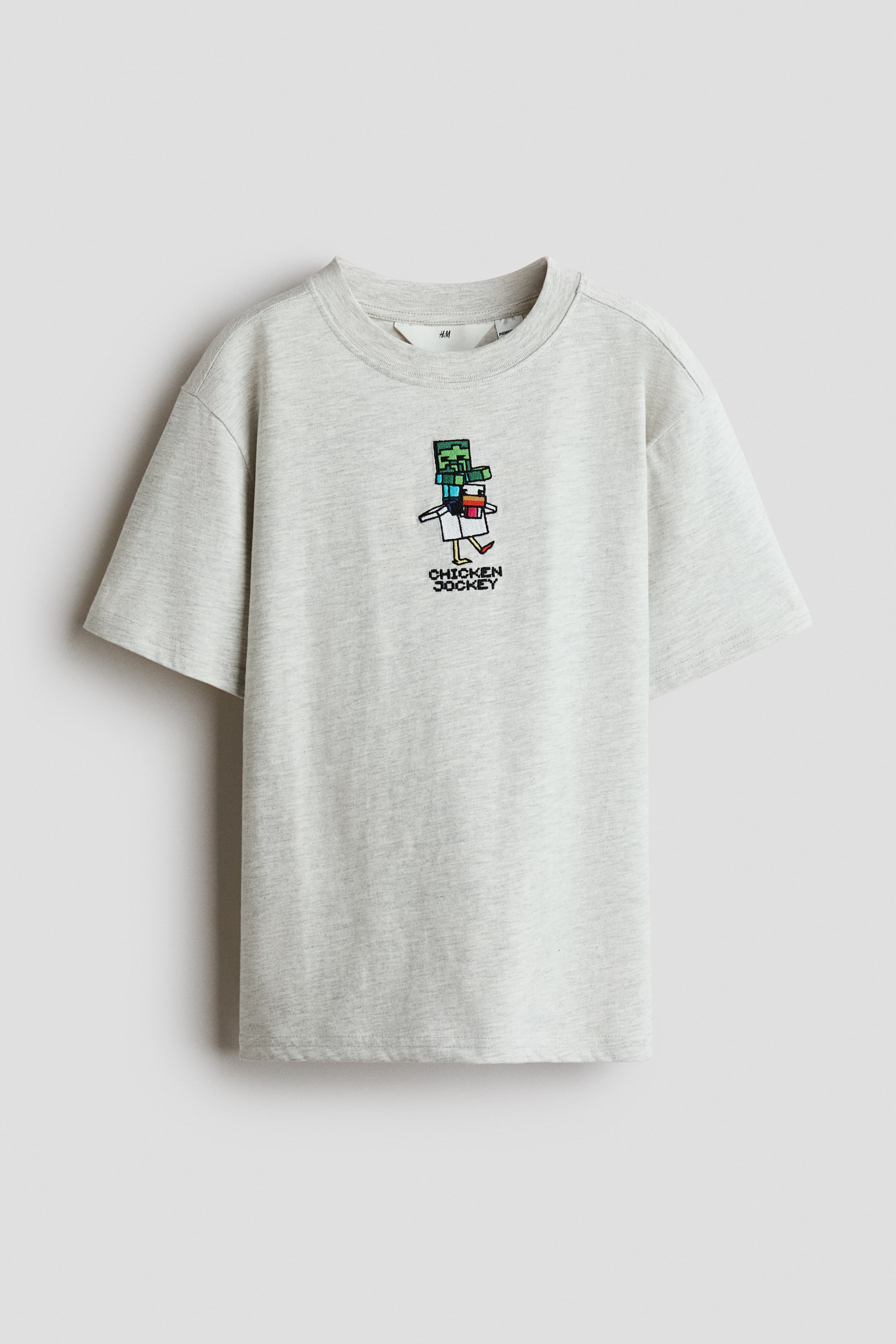 Преглед на по-голямо изображение: Светлосив памучен джърси T-shirt с кръгло рипсено деколте, къси ръкави и прав подгъв. Върху предната част е изобразен пикселизиран графичен принт на персонаж, яздещ кокошка, с надпис „CHICKEN JOCKEY“ отдолу.