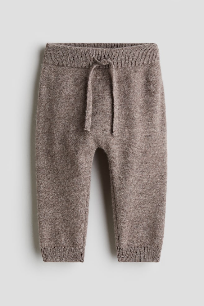 Brown knitted trousers are displayed from the front, featuring a ribbed, elasticated waist with a tied drawstring and ribbed cuffs. - 1