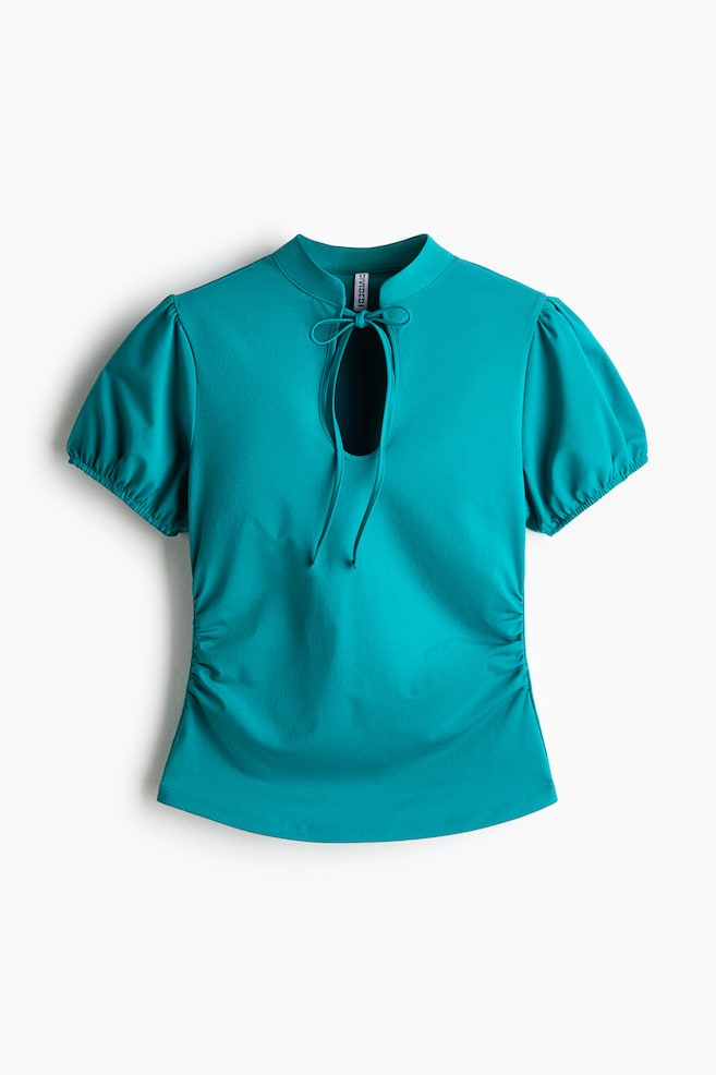 A teal-colored fitted top is shown facing front, featuring a band collar with a large keyhole opening and narrow ties tied at the neck. The top is displaying short puff sleeves with elasticated cuffs, gathered side seams at the waist, and a gently rounded hem. - 1