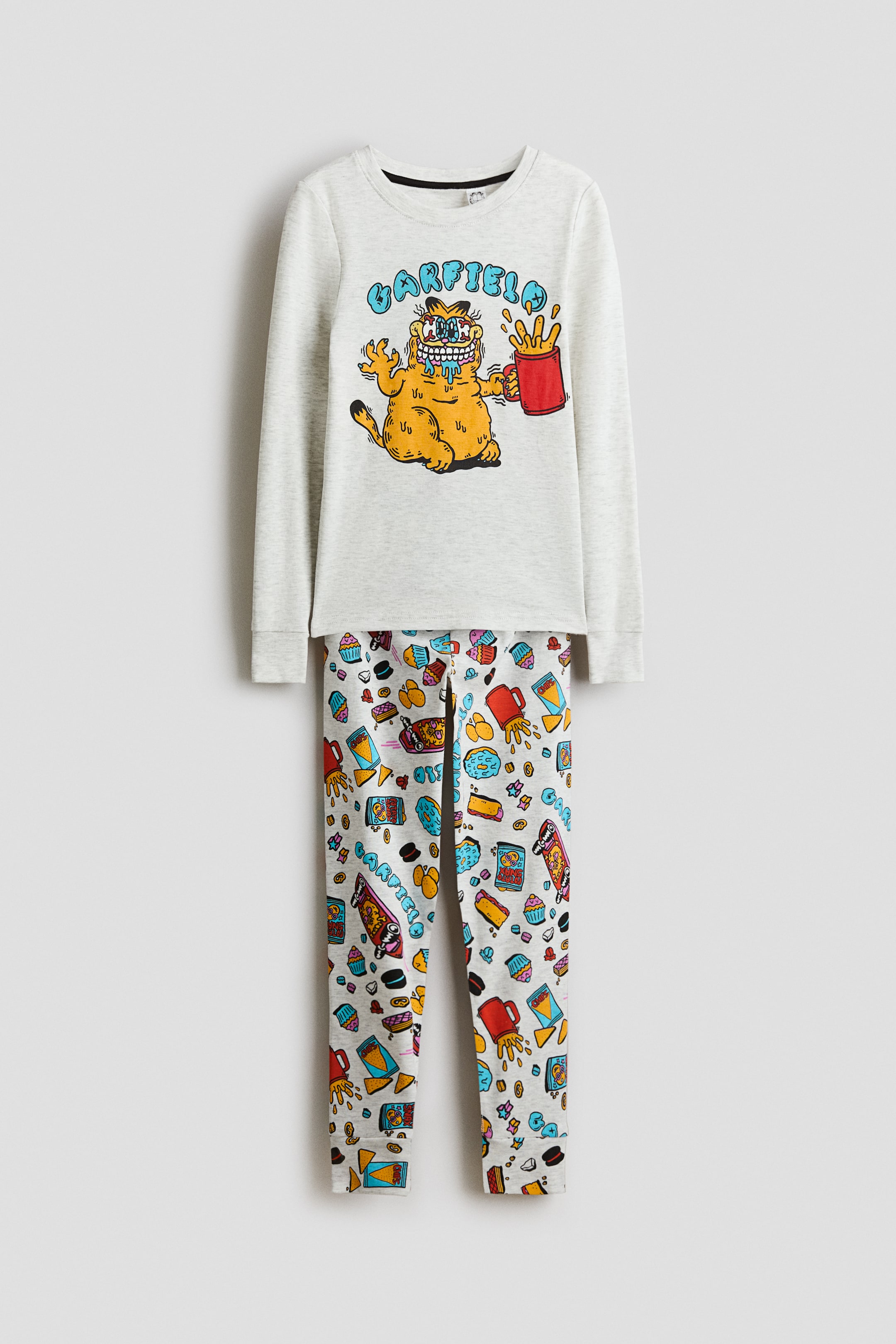 Voir une image plus grande: Un ensemble de pyjama gris chiné, vu de face, comprend un haut à manches longues et un pantalon long coordonné. Le haut affiche un visuel de Garfield bavant tenant un contenant rouge de frites, avec "GARFIELD" en lettres bulles bleues au-dessus, tandis que le pantalon présente un motif imprimé sur l'ensemble composé de divers aliments et du texte "GARFIELD".