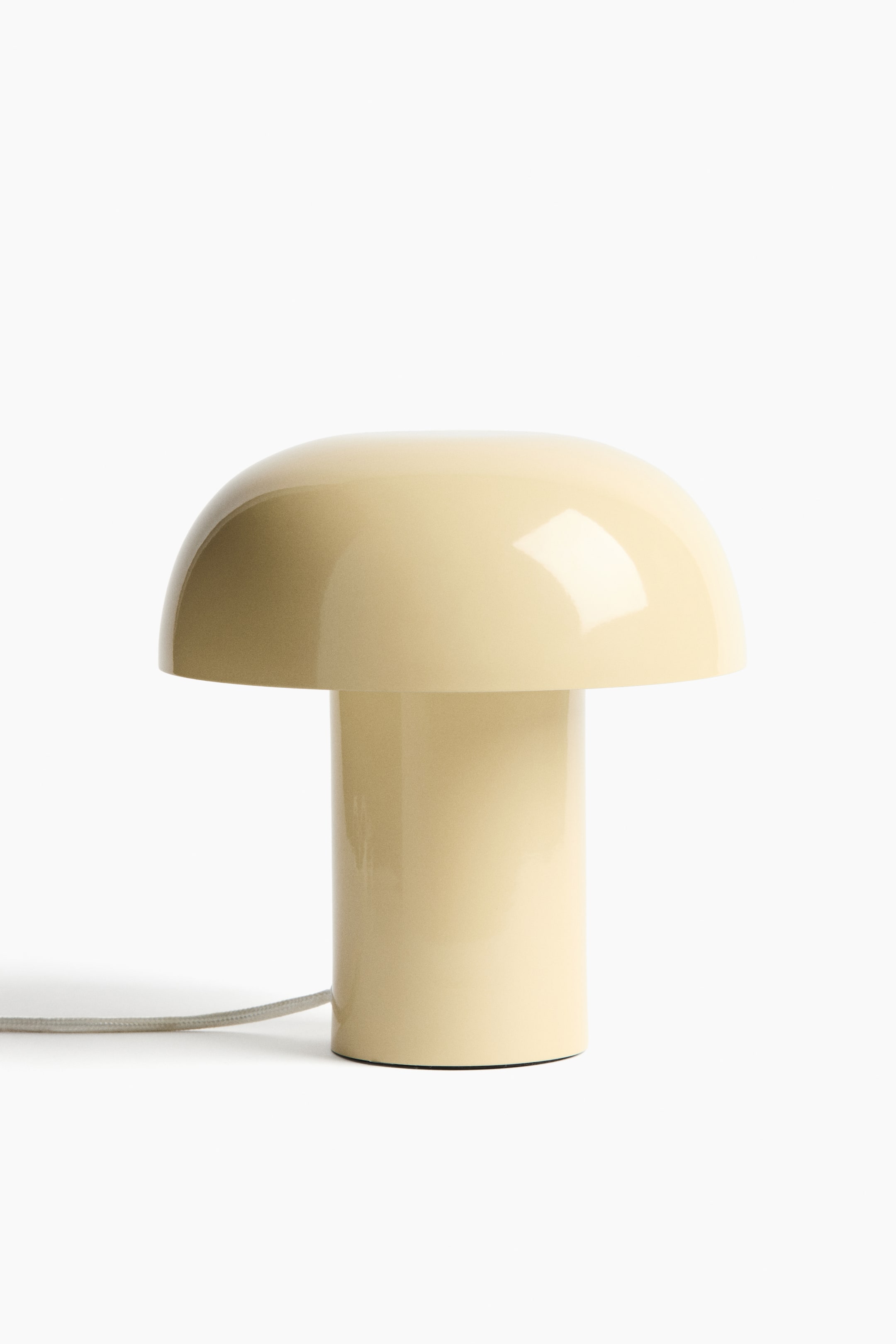 Agrandir l'image: Cette lampe de table moderne est conçue en forme de champignon et présente une finition métallique brillante couleur jaune crème. Un cordon gris clair, gainé de tissu, sort de sa base cylindrique.