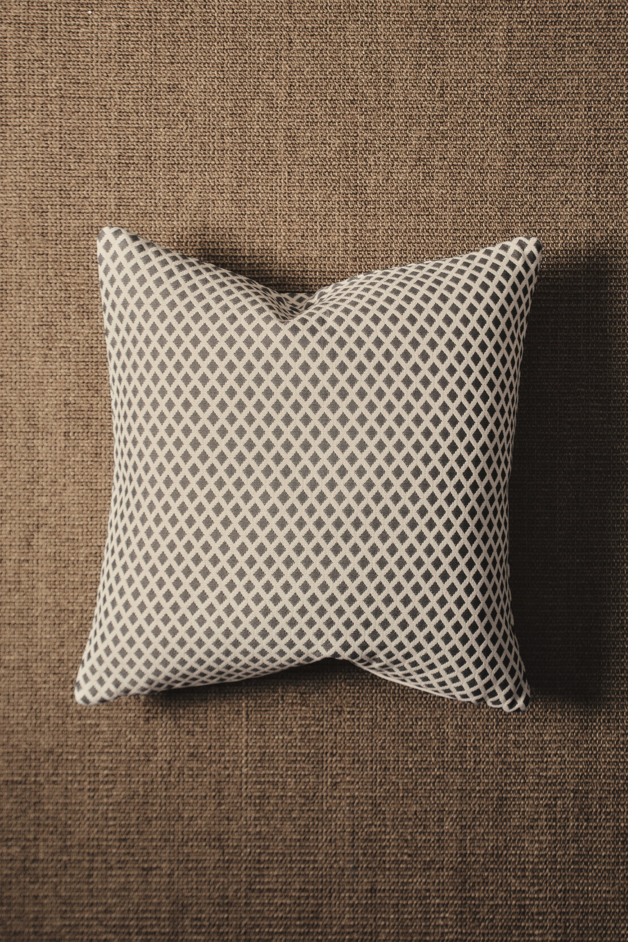 View larger image: The cushion cover showcases a textured pattern of dark gray diamonds on a light gray background, appearing plump from a top-down view.