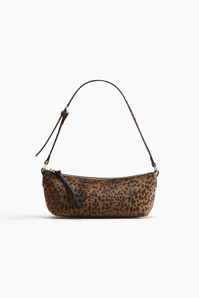 A front-facing leopard print handbag is featuring an elongated, structured body, a single adjustable strap with gold-toned hardware, and a top zipper closure with a black pull tab. - 1