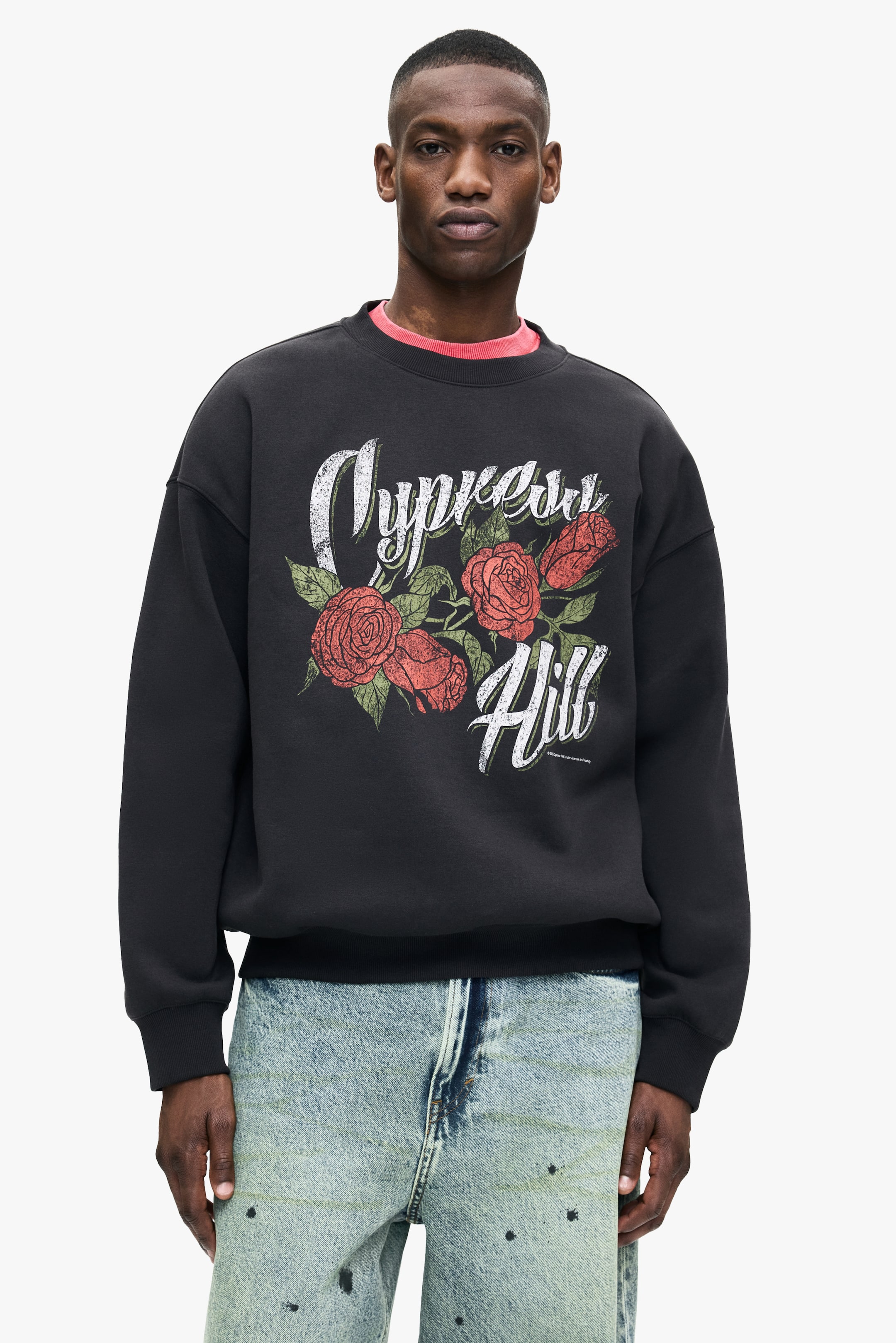 View larger image: A black oversized crew-neck sweatshirt, featuring a distressed "Cypress Hill" graphic with red roses and green leaves, is being worn by the model. A coral t-shirt is being layered underneath.