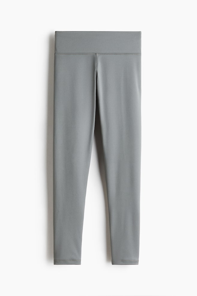 Leggings de sport gris présentés à plat, face avant, avec un tissu lisse et mat. Ils sont conçus avec une large ceinture haute, des coutures plates apparentes et une longueur raccourcie. - 1