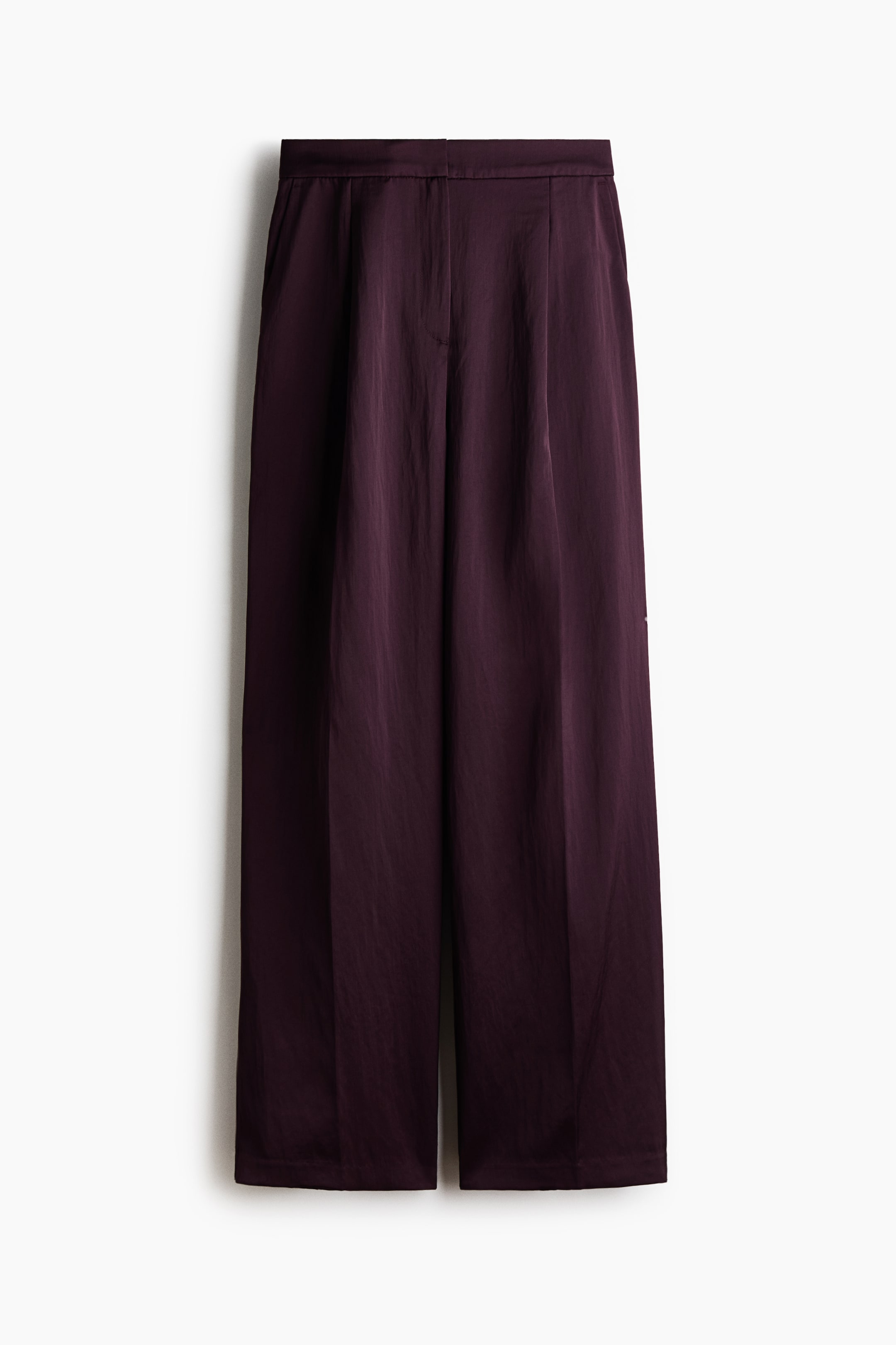 View larger image: Wide-leg trousers in a dark plum hue are shown from the front, featuring a high waist with front pleats and pressed creases running down the legs. The trousers showcase a gently crinkled texture, a clean waistband with a concealed front closure, and diagonal side pockets.