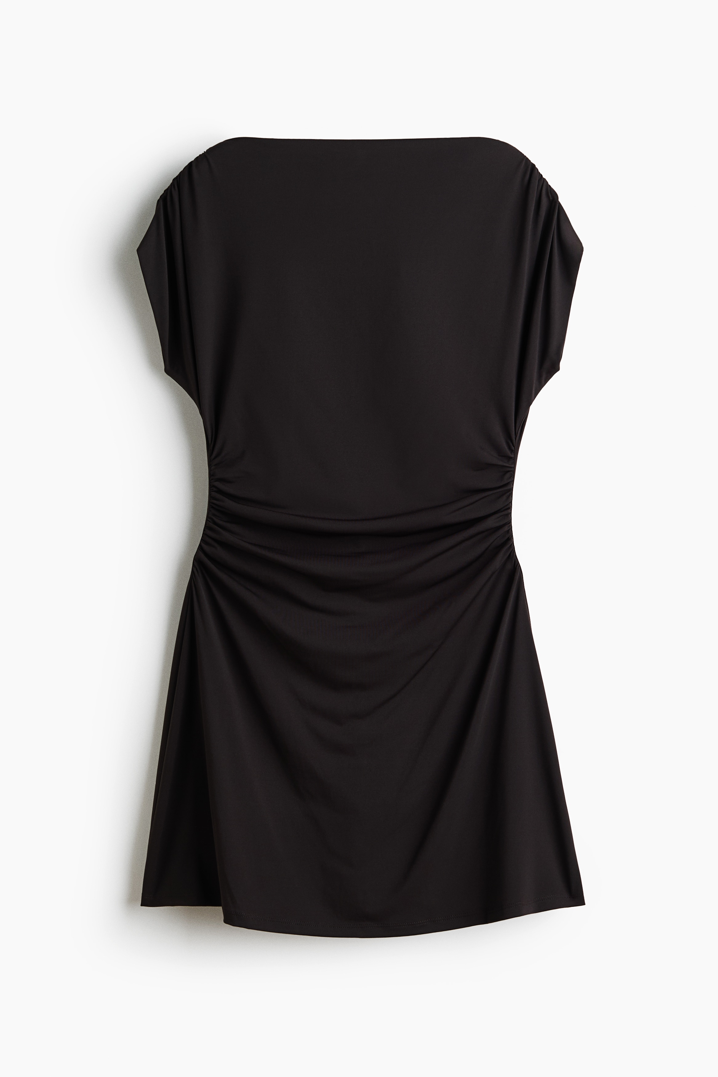La modelo lleva puesto un vestido corto de jersey color café oscuro, con cuello barco alto, mangas tipo capa y costuras laterales fruncidas que crean un efecto drapeado sobre la cintura. El vestido se ajusta al cuerpo y presenta un dobladillo de corte recto.