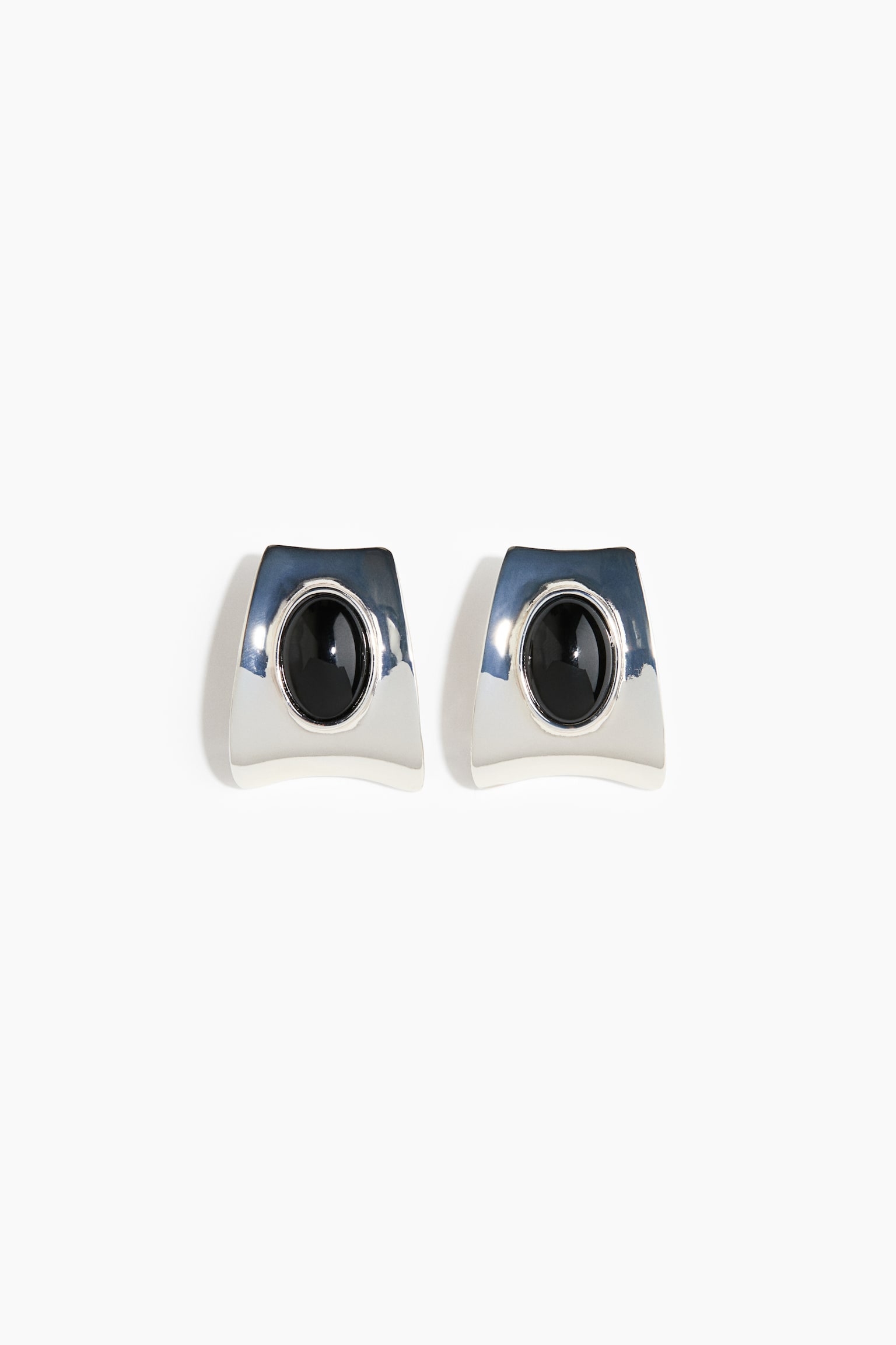 Et par Ã¸reringe i sÃ¸lvfarvet tone med en buet, trapezformet silhuet og en hÃ¸jt poleret metallisk finish. Hver Ã¸rering har en centralt placeret, bezel-indfattet oval sort cabochon-sten. - 1