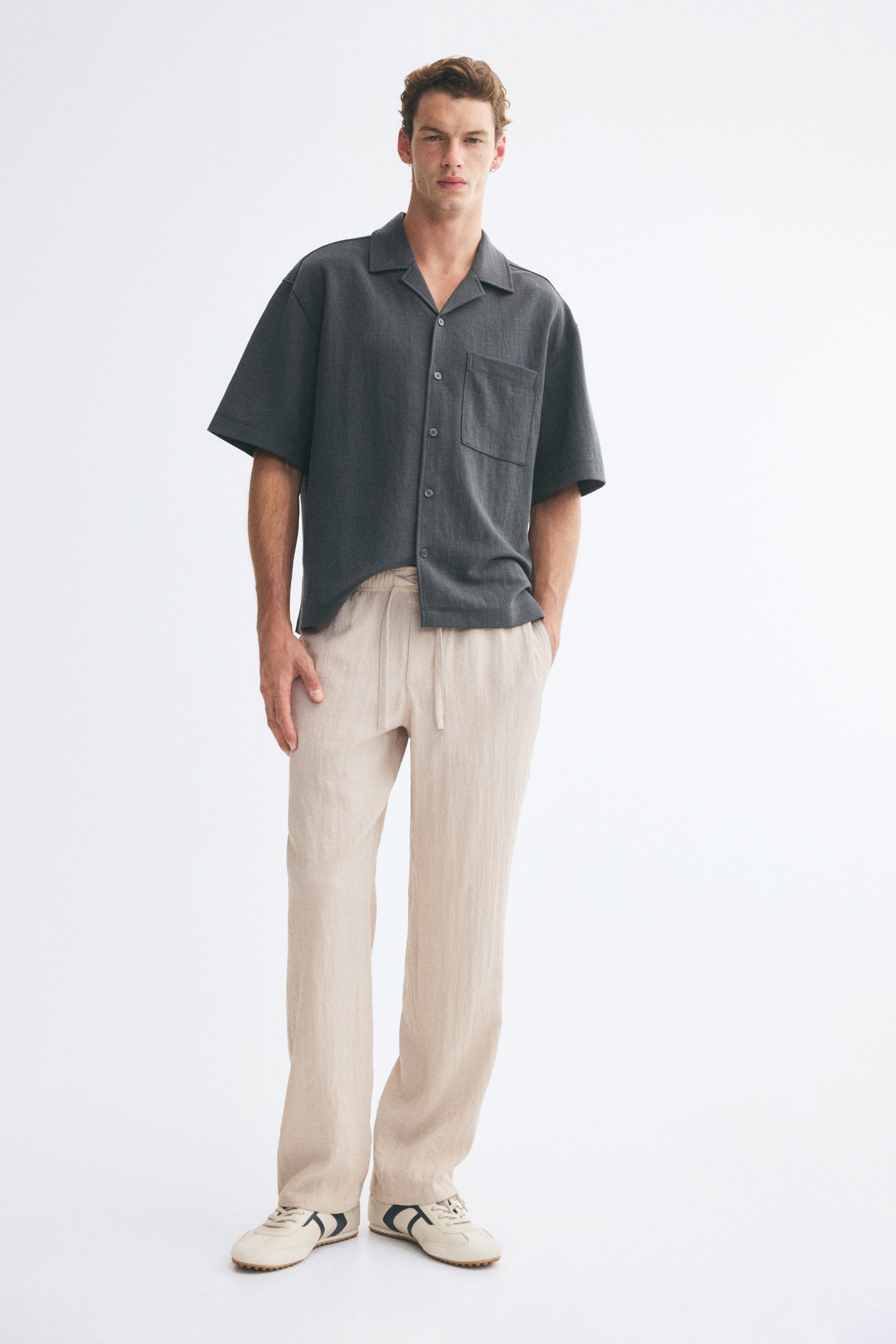 These light beige straight-leg pants are displayed in a front-facing view, highlighting the crinkled fabric texture and relaxed fit. The pants feature an elasticated waistband with an adjustable drawstring, a mock fly detail, and discreet side seam pockets.