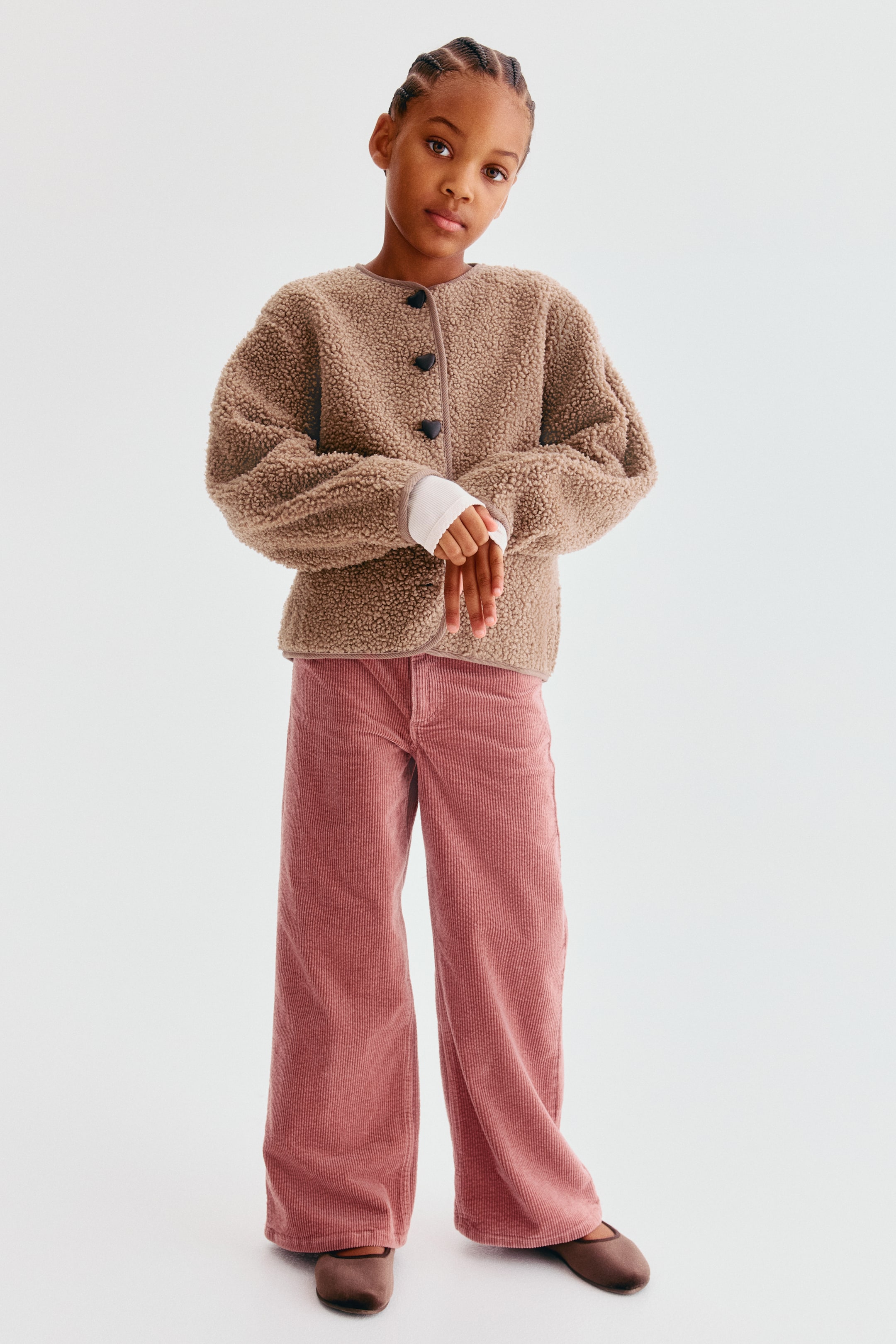 Agrandir l'image: Vue de face du pantalon large en velours côtelé rose poudré, mettant en valeur sa coupe décontractée et son tissu texturé à côtes. Le pantalon tombe souplement jusqu’aux pieds, soulignant sa silhouette droite et ample.
