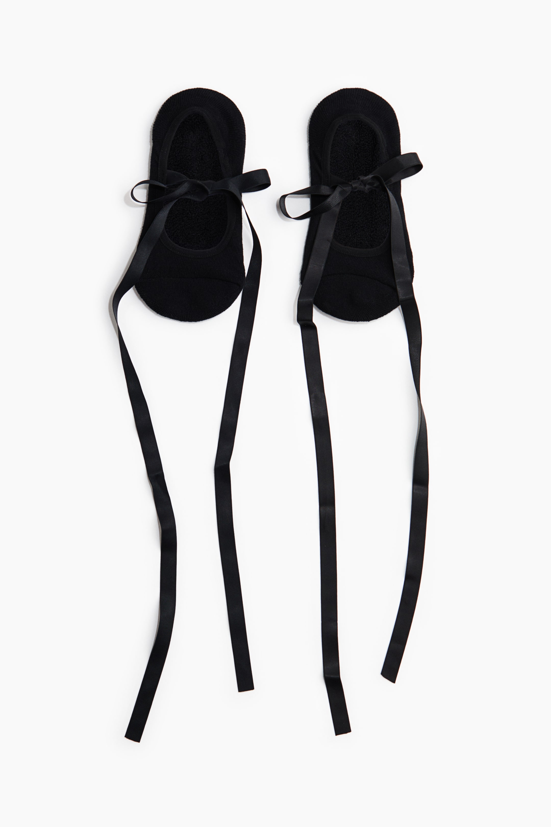 View larger image: A pair of black footie socks features long black ribbons tied in bows across the instep of each sock, with the ribbons extending downwards.