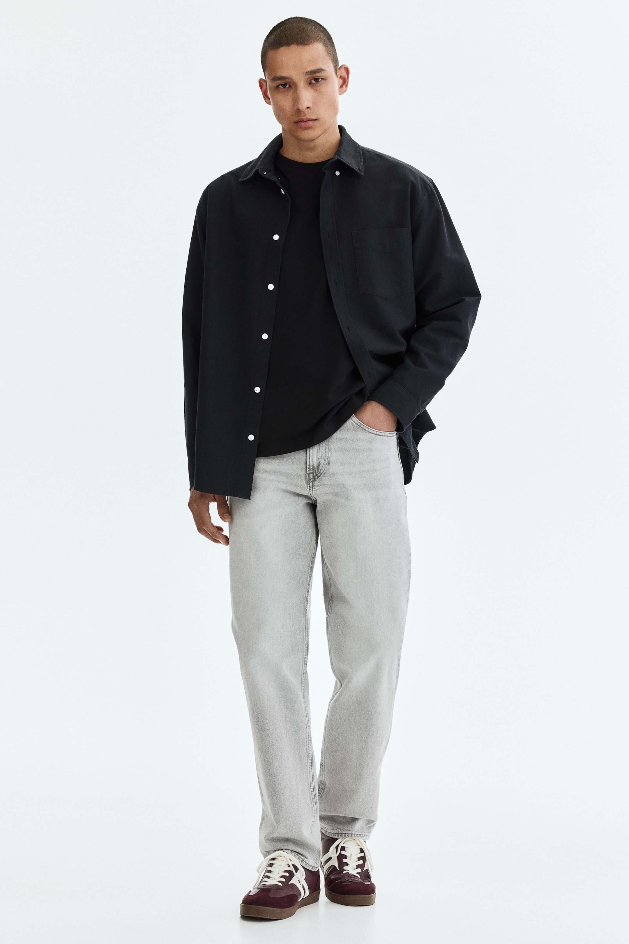Ver imagen más grande: La camisa negra abotonada está orientada hacia adelante, con un cuello en punta, mangas largas y botones blancos a lo largo de la tapeta frontal. Muestra un único bolsillo de parche en el pecho izquierdo y se lleva abierta sobre una camiseta negra de cuello redondo.
