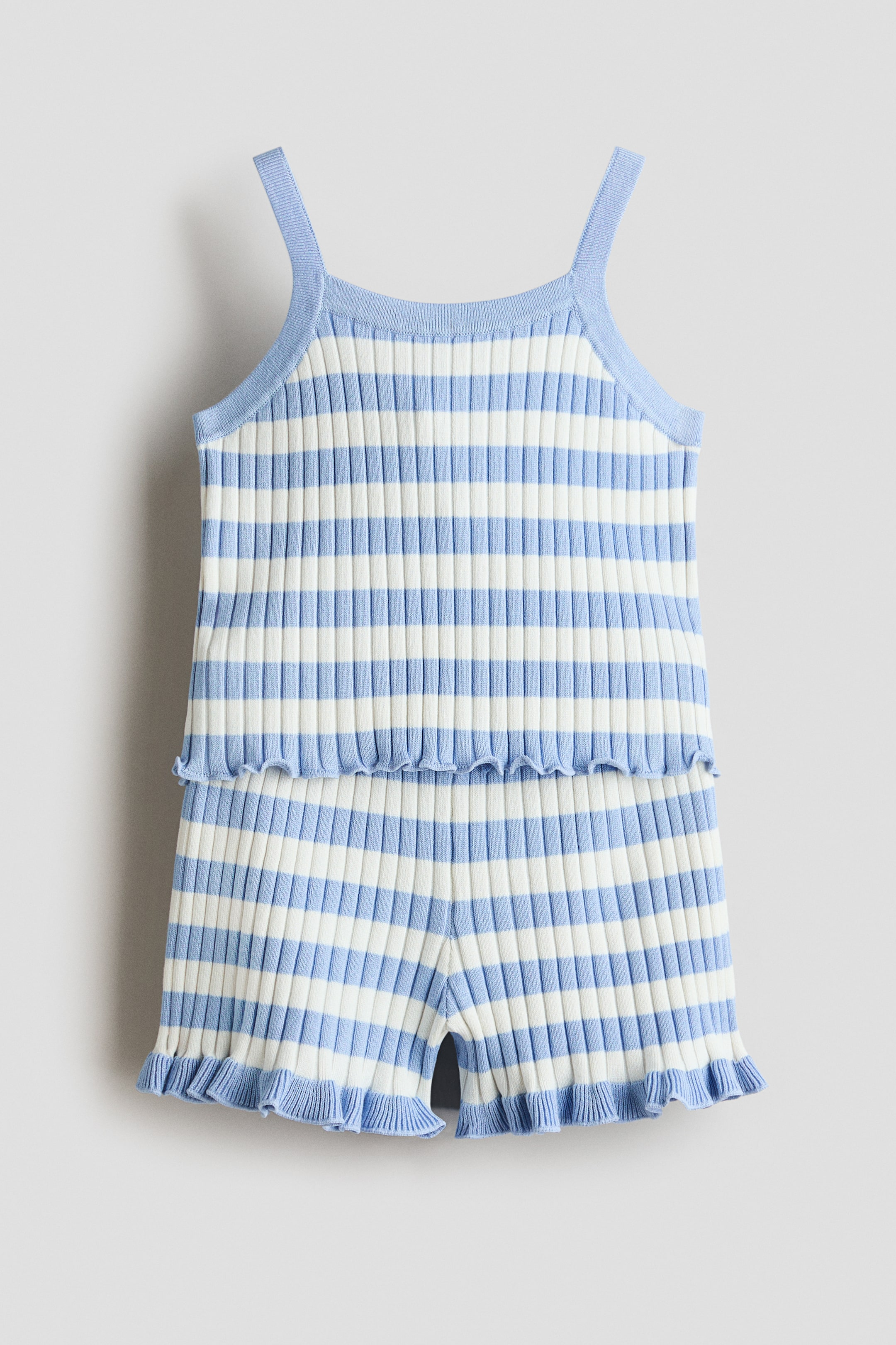 View larger image: A two-piece, ribbed-knit set featuring light blue and off-white horizontal stripes, presented from the front. The camisole top showcases thin straps and a frilled hem, while the matching shorts display frilled leg openings with small side slits.