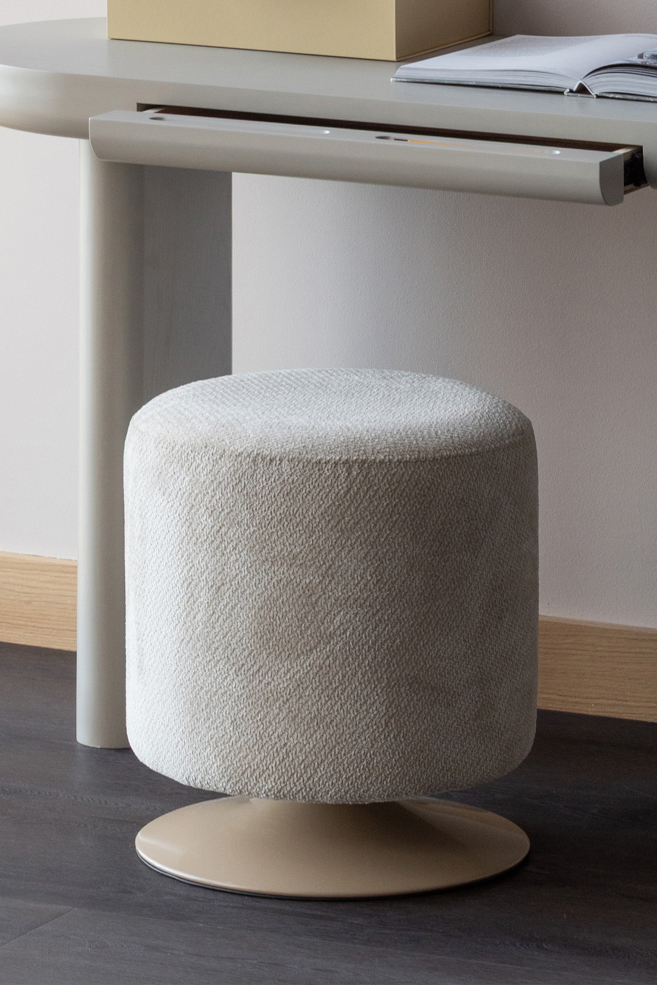 Grotere afbeelding bekijken: Een cilindrische poef is bekleed met een lichtbeige, gestructureerde stof en rust op een ronde, vlakke, matte tan basis.