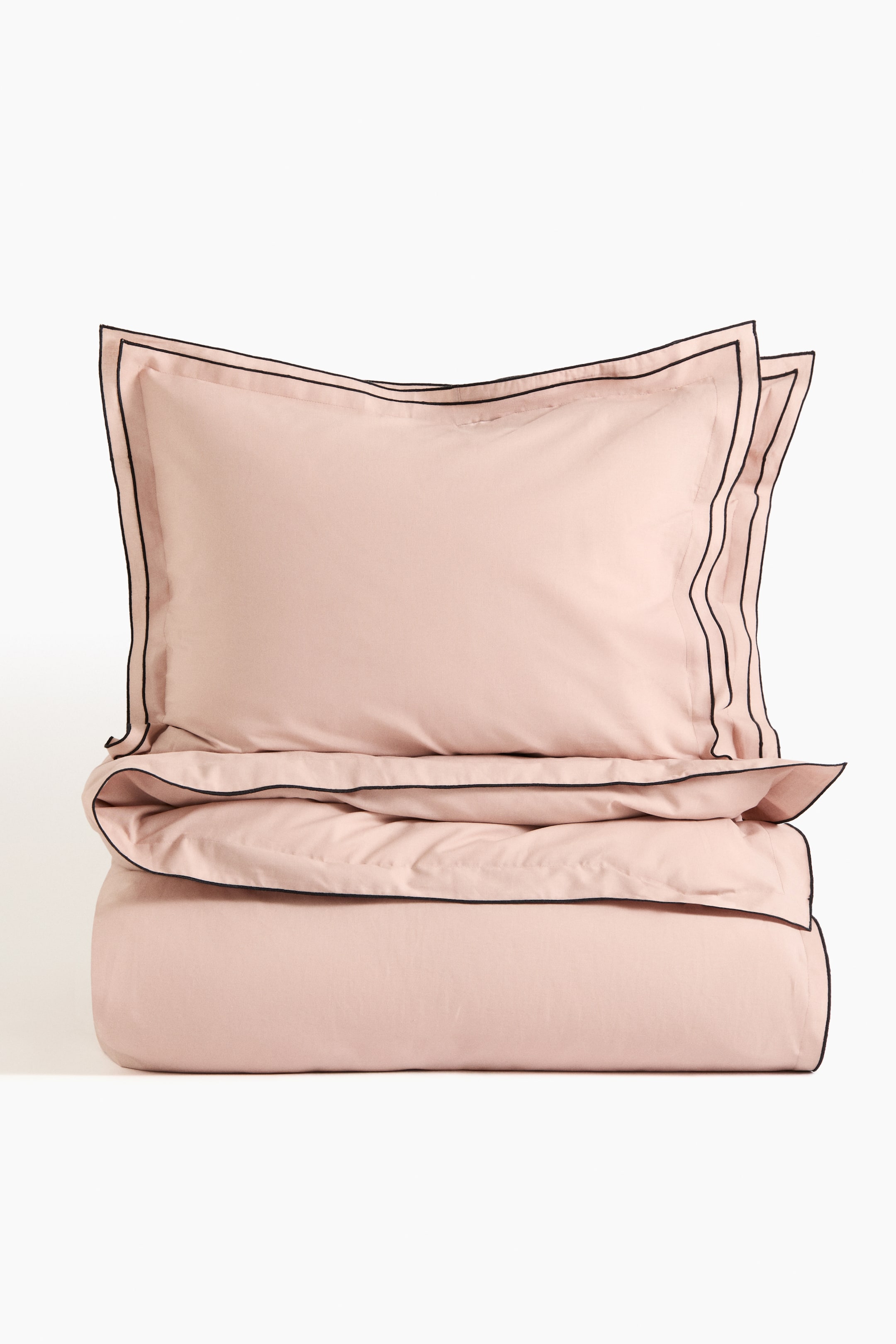 View larger image: A double/king duvet cover set is presented, featuring a light-pink pillowcase with a double-winged border and a folded duvet cover with a single-wing border. Both borders are detailed with black piping.