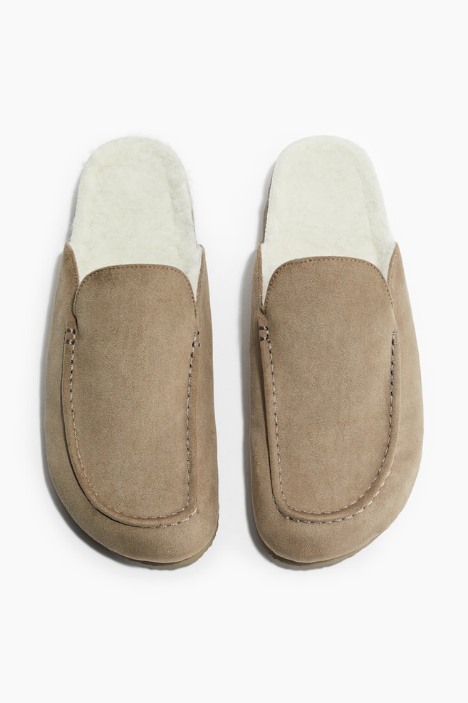 Une vue de face montre une paire de mocassins en daim couleur tan. Chaque mocassin présente un bout cousu et une doublure moelleuse de couleur crème visible qui s'étend au-dessus de l'ouverture. - 1