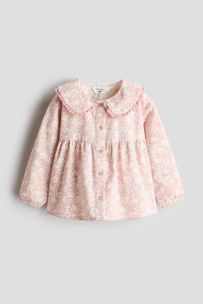Une blouse en velours cÃ´telÃ© Ã  coupe dÃ©contractÃ©e, avec un imprimÃ© floral rose et blanc, est prÃ©sentÃ©e de face, dotÃ©e dâun col Claudine bordÃ© de dentelle et dâune ouverture boutonnÃ©e sur le devant. La blouse prÃ©sente une couture froncÃ©e sous la poitrine, qui apporte du volume au corps, ainsi que des manches longues avec poignets Ã©lastiquÃ©s. - 1