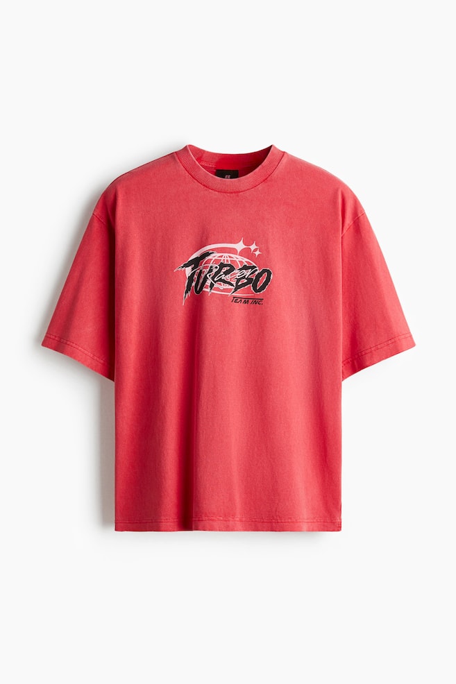 Een rood t-shirt met een gewassen look wordt van voren getoond, met een centraal printmotief, een ronde halslijn met ribboord, verlaagde schouders en een recht gesneden zoom. Het t-shirt heeft een losse pasvorm en de centrale print toont een gestileerde "TURBO" tekst boven "TEAM INC.", vergezeld van een wereldbolgrafiek. - 1