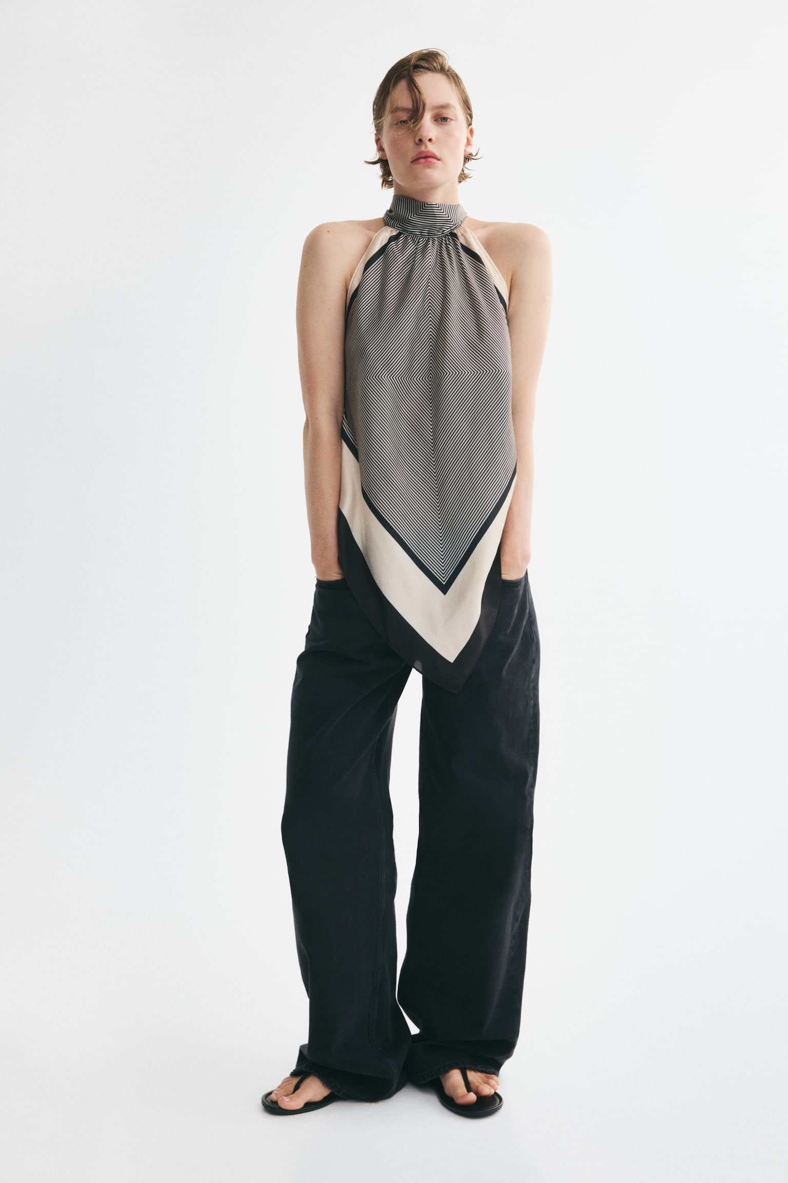 A diamond-shaped scarf, fashioned as a top, is hanging, showcasing a black and white diagonal striped pattern forming chevron shapes. It features wide cream borders accented by a thin black edge, and its top is gathered, hinting at a halter neckline. - 1