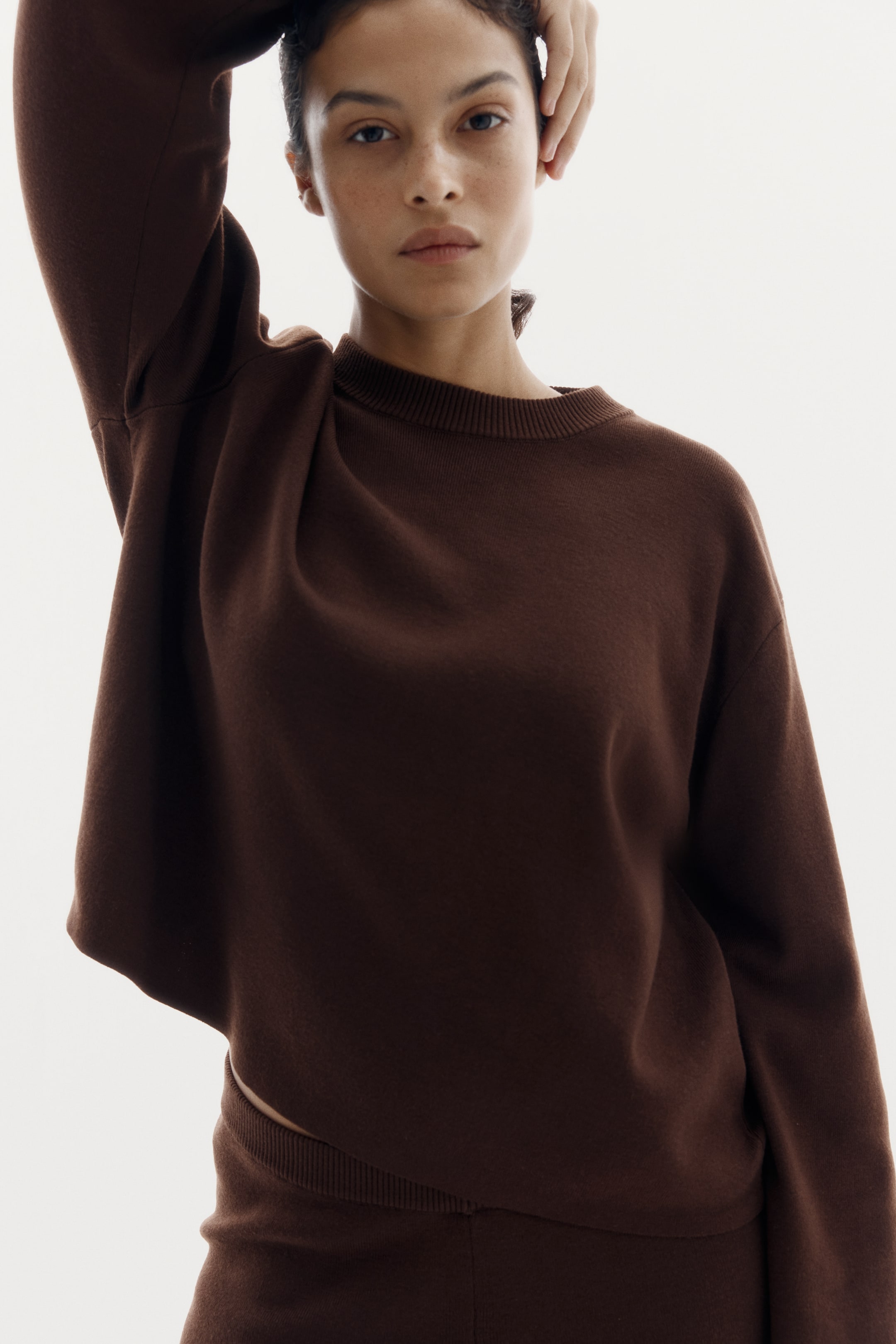 Voir une image plus grande: Un haut en tricot à manches longues et col rond de couleur brun foncé, doté d'un col côtelé, est porté avec un bas en tricot assorti de couleur brun foncé, qui présente une taille côtelée visible.