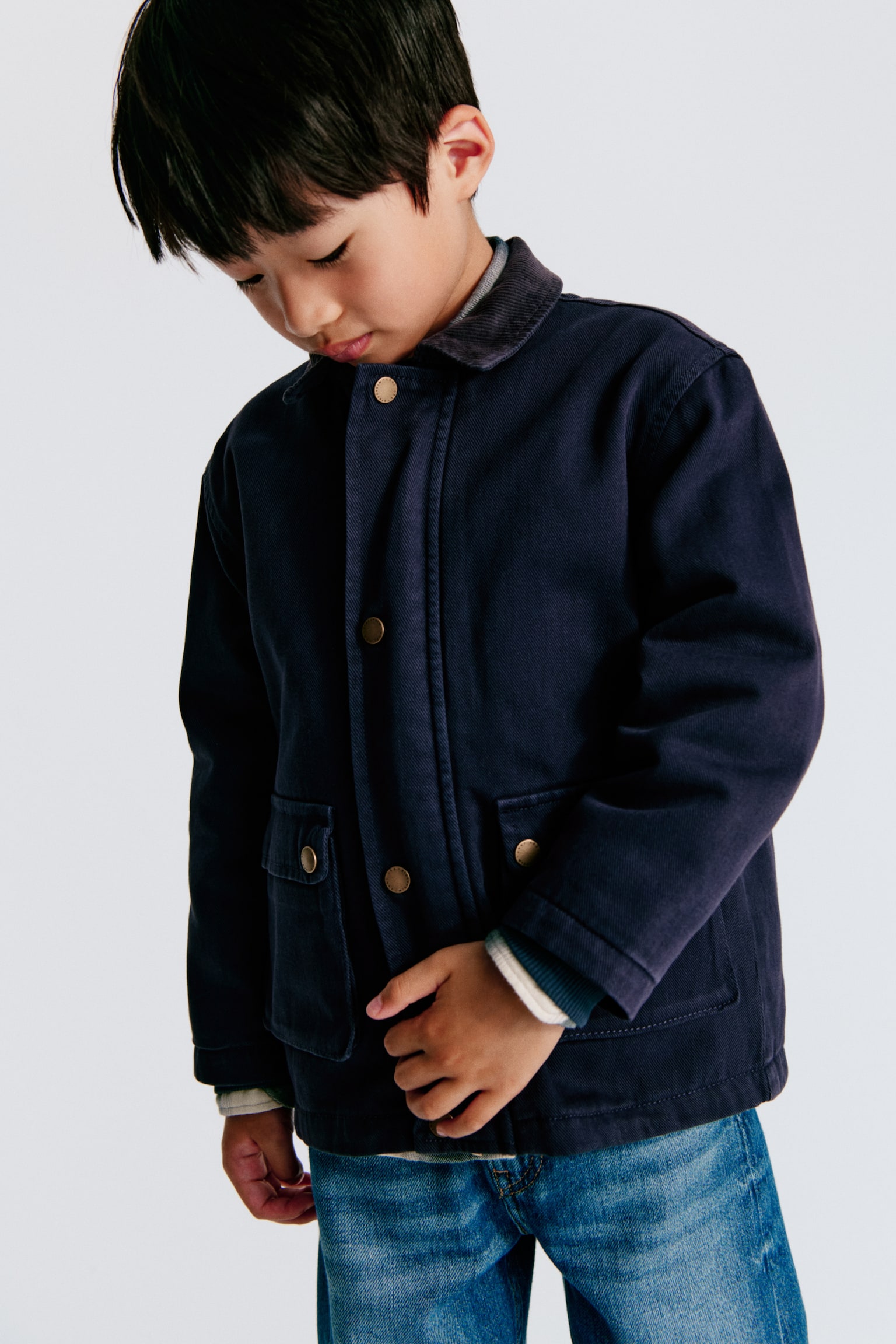 A dark blue jacket is facing forward, featuring a dark blue corduroy collar and a front placket with gold-toned snap fasteners. Two large patch pockets are visible on the lower front, each with a flap secured by a gold-toned snap fastener. - 1