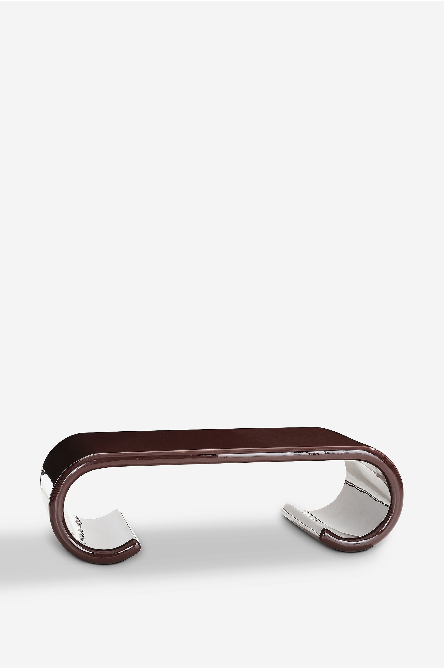 Een moderne salontafel, weergegeven vanuit een frontale driekwartshoek, heeft een sculpturaal ontwerp met een hoogglanzende, diepbruine afwerking en naar binnen gebogen poten in scrollvorm die een sterk reflecterende zilverkleurige onderzijde onthullen. Rechts op het vlakke tafelblad rust een kleine potplant in een metalen schaal bovenop twee boeken.