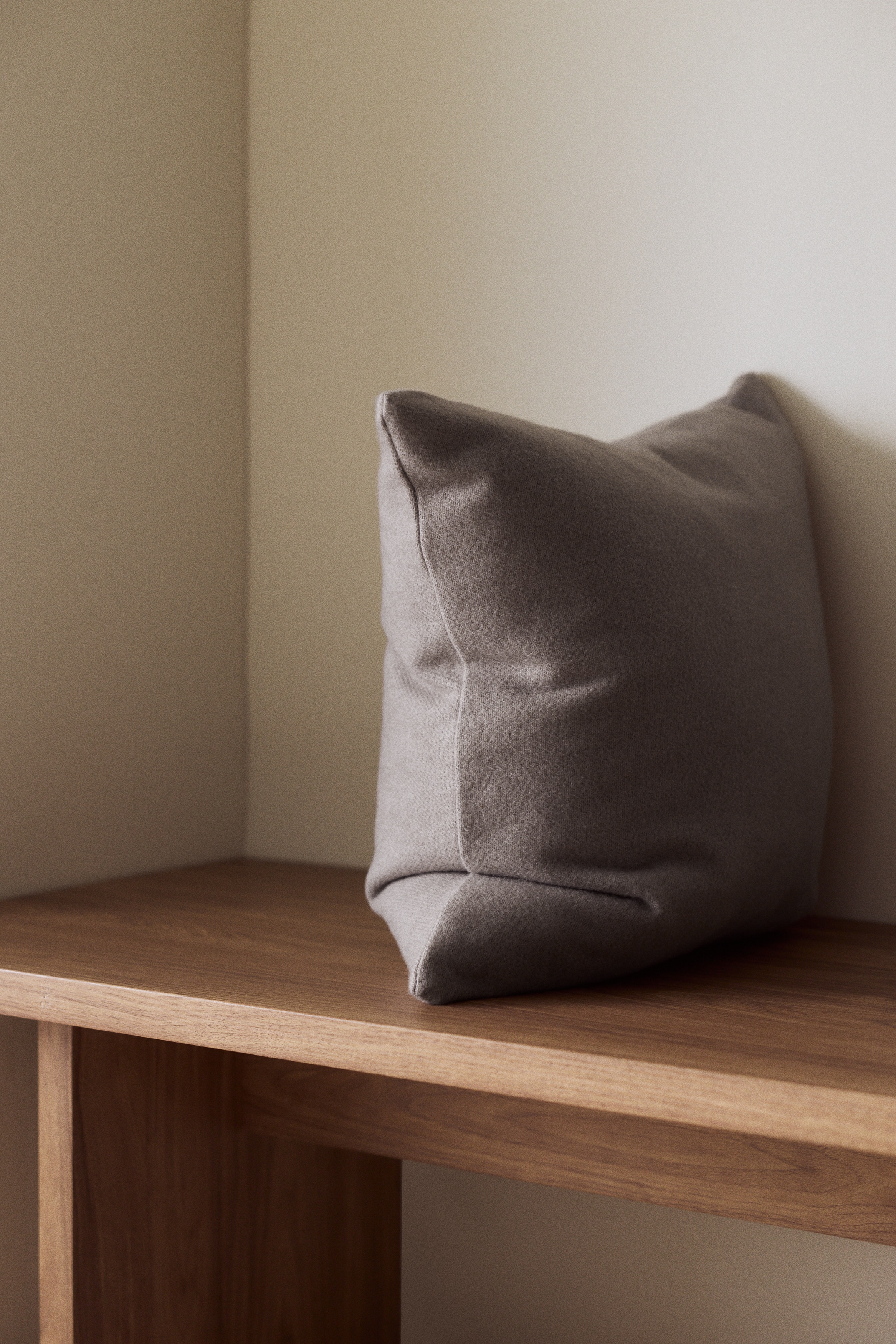 Ein quadratisches Kissen präsentiert seine taupe-graue Farbe, den weichen, dezent strukturierten Stoff und die pralle Form.