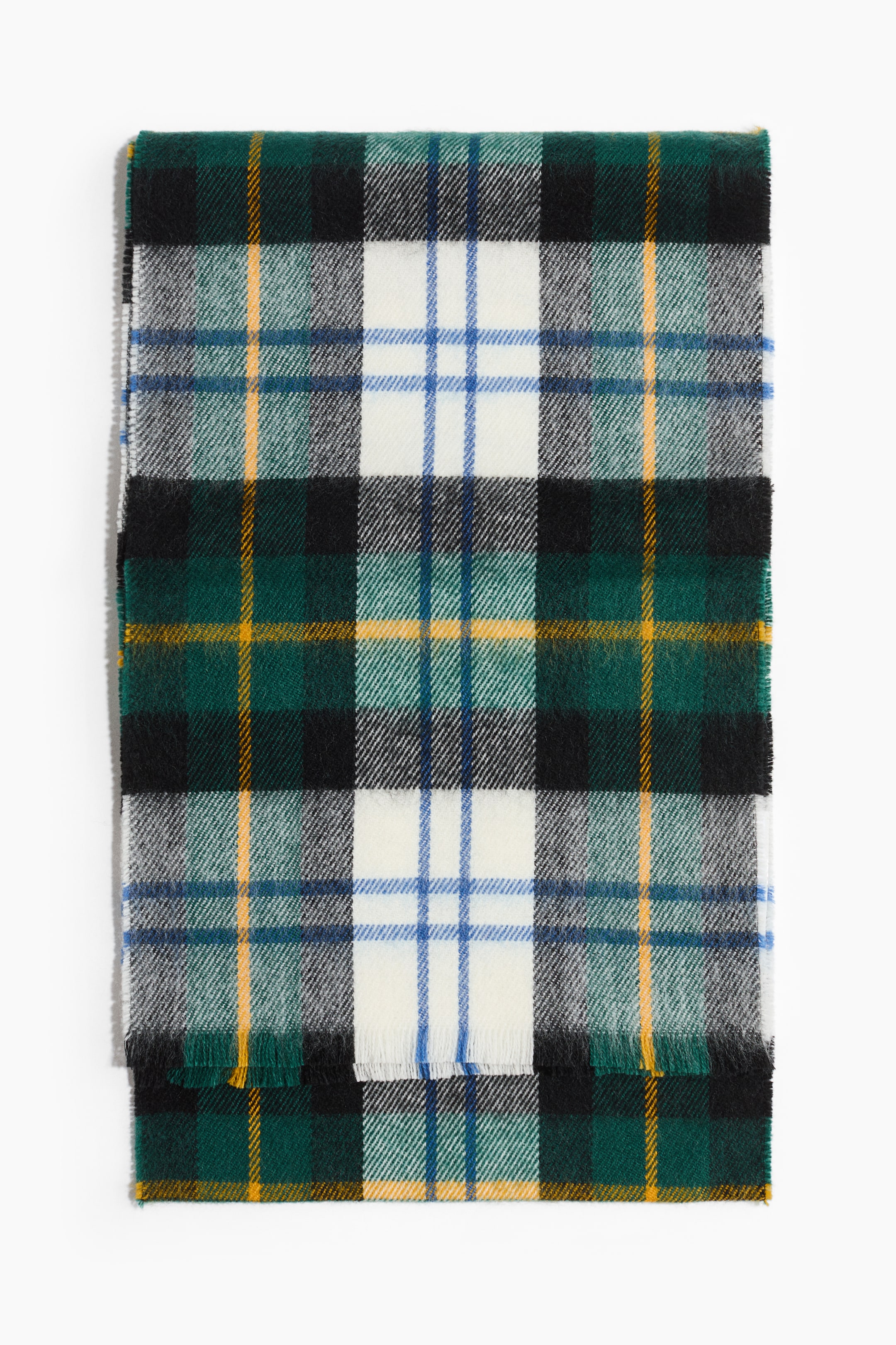 View larger image: A tartan scarf is lying flat, folded lengthways. It displays a grid pattern with dark green, black, white, blue, and yellow lines, and fringed edges are visible at the bottom.