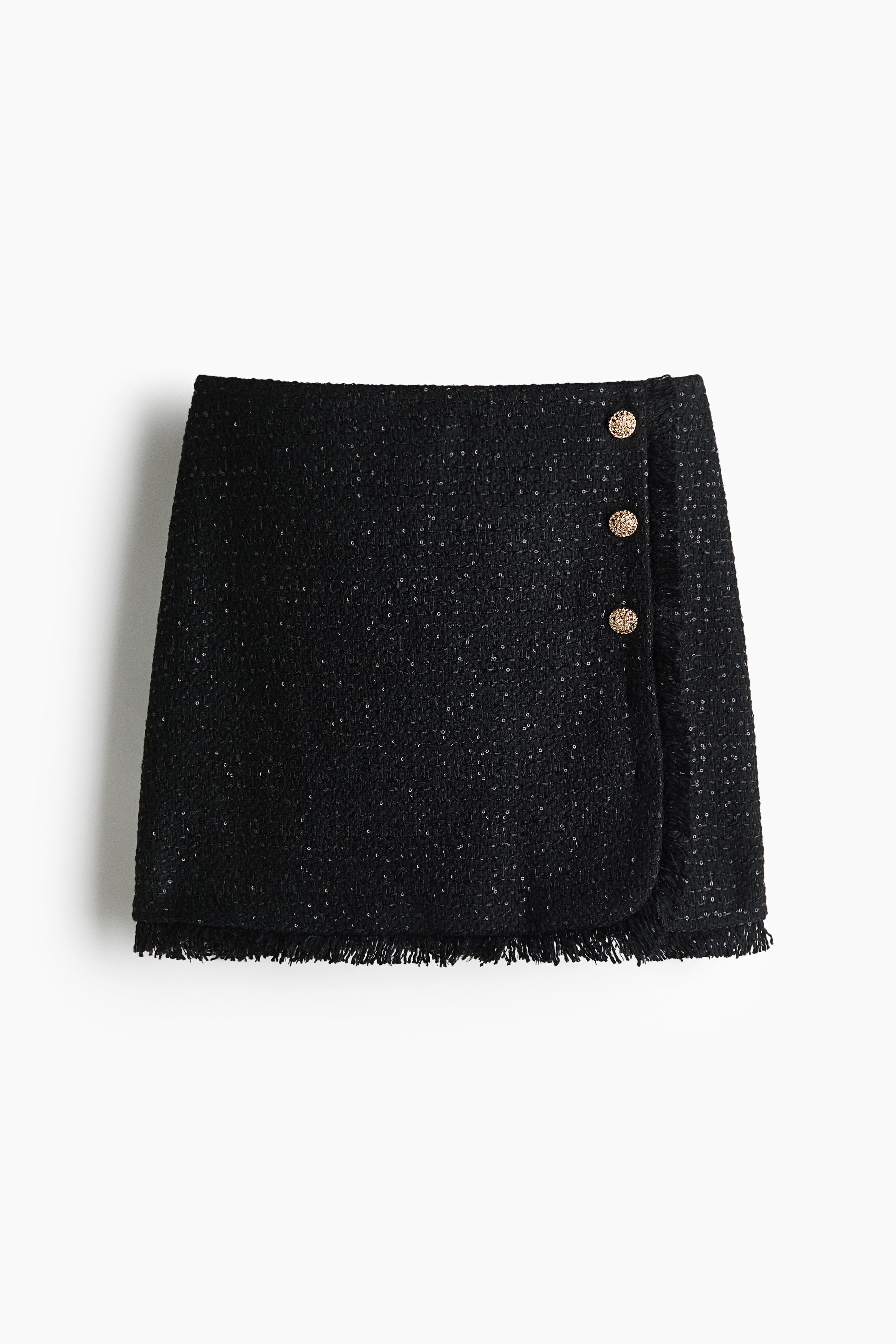 A white long-sleeved button-down shirt with a pointed collar is being worn by the model, tucked into a black textured mini skirt with decorative side buttons. The shirt is styled with an open collar as the model stands with hands resting on hips.