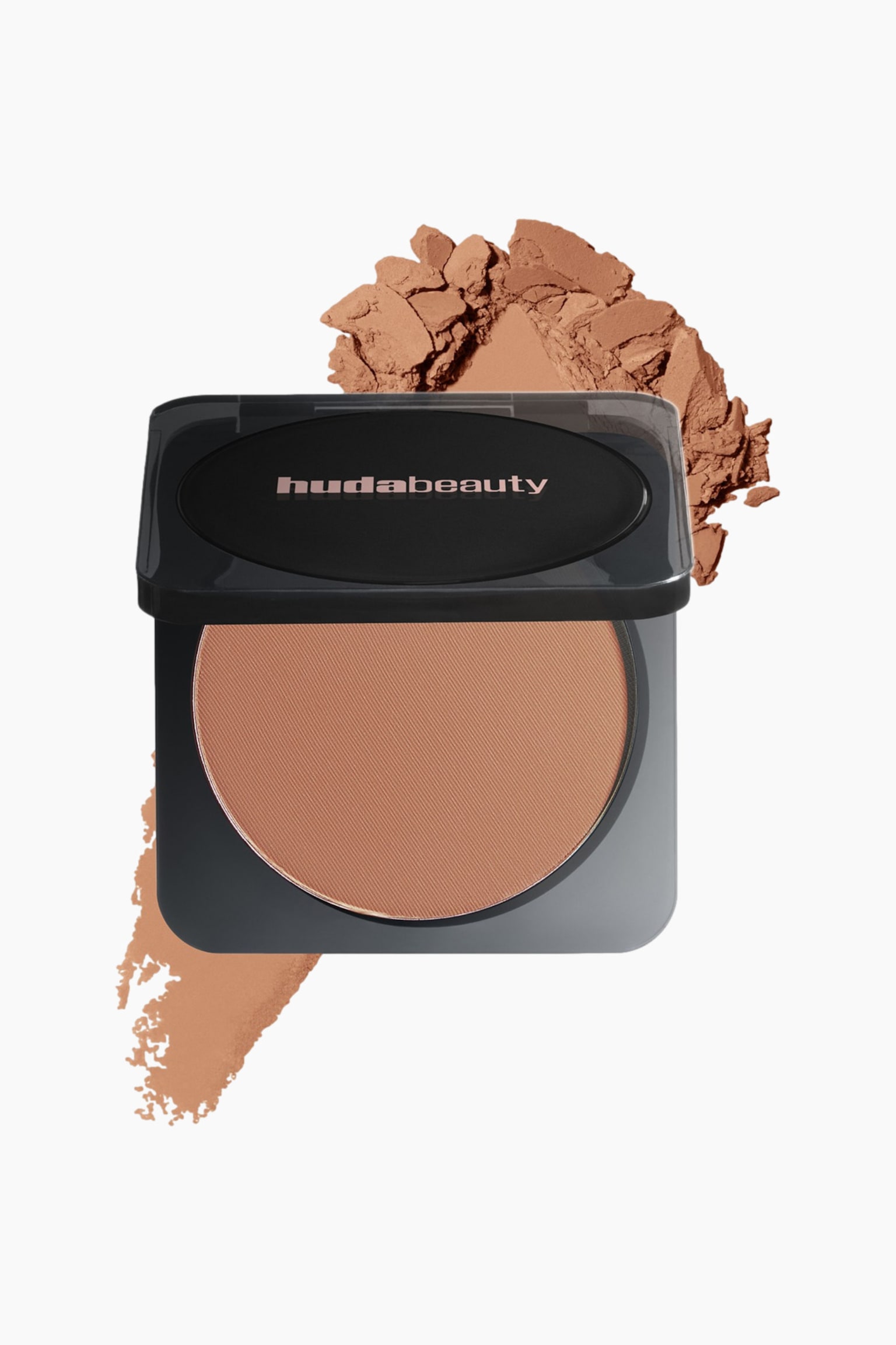 Huda Beauty -kompaktipuuteri avautuu ja paljastaa pyöreän, vaaleanruskean puristetun puuterin pannun, jossa on hienojakoinen koostumus. Mustassa kompaktissa kannessa lukee "hudabeauty" ja se on hieman kallistettu; sen takana lepää irtopuuteria ja alapuolelle ulottuu tuotteen sävynäyte.