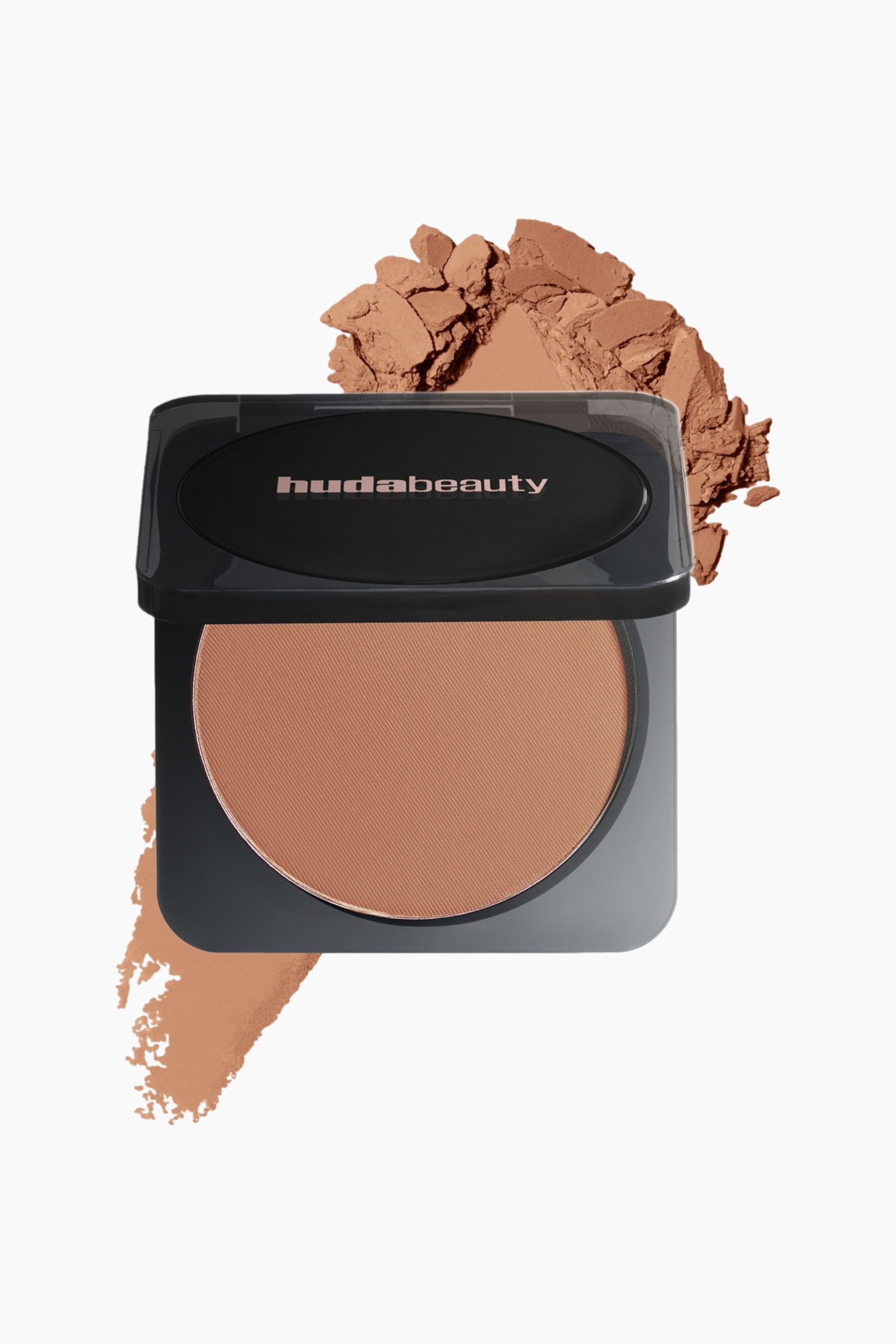 Vis større bilde: Et Huda Beauty kompaktpudder åpnes og viser en rund beholder med beige, presset pudder med fin tekstur. Den svarte kompakten har "hudabeauty" på lokket og står svakt vinklet, med løst pudder bak den og en fargeprøve som strekker seg nedenfor.