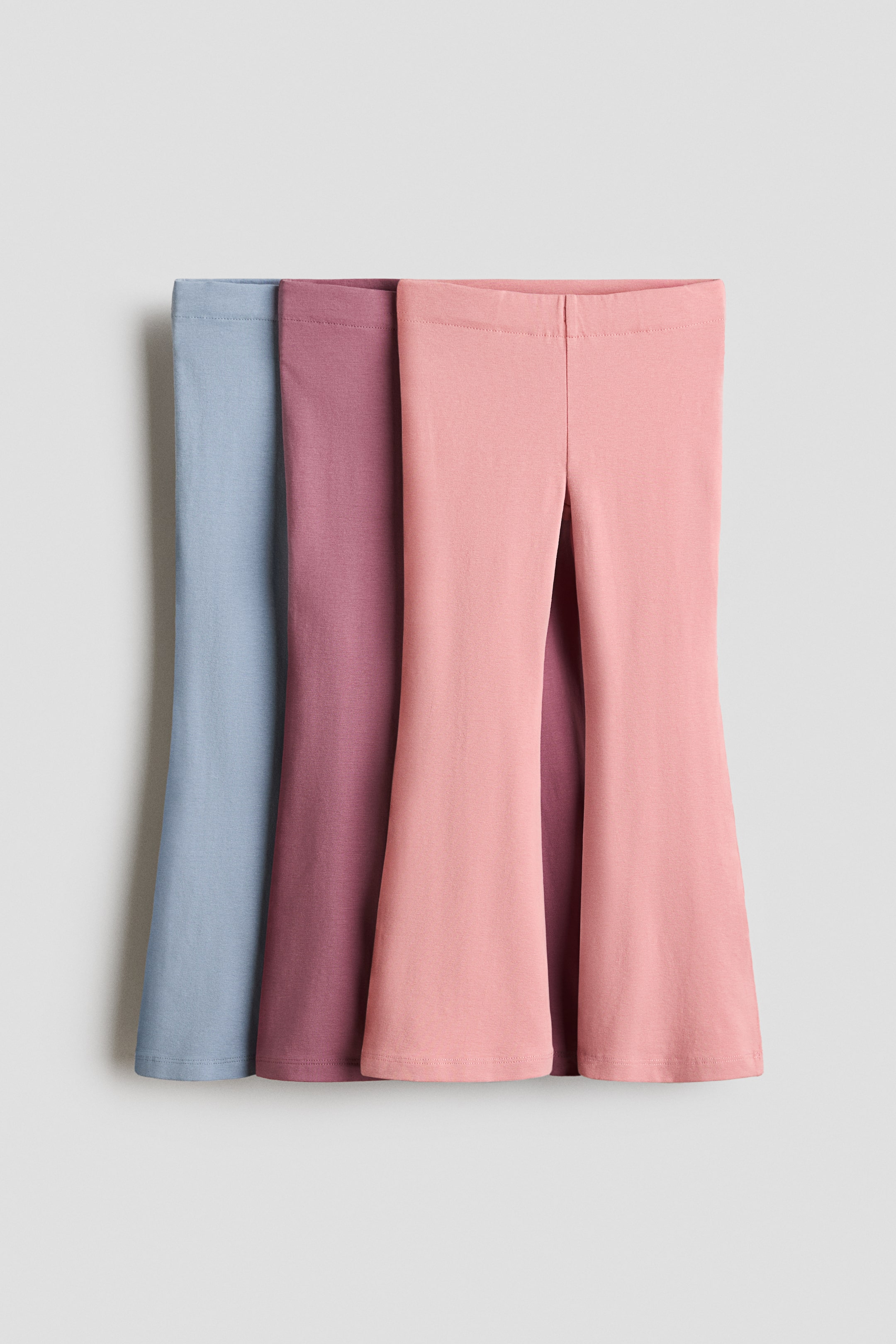 Se større billede: Tre par leggings præsenteres forfra og fremhæver deres bløde bomuldsjersey. Hvert par er designet med elastisk talje og vide ben og fås i lyseblå, støvet rosa og lyserød.