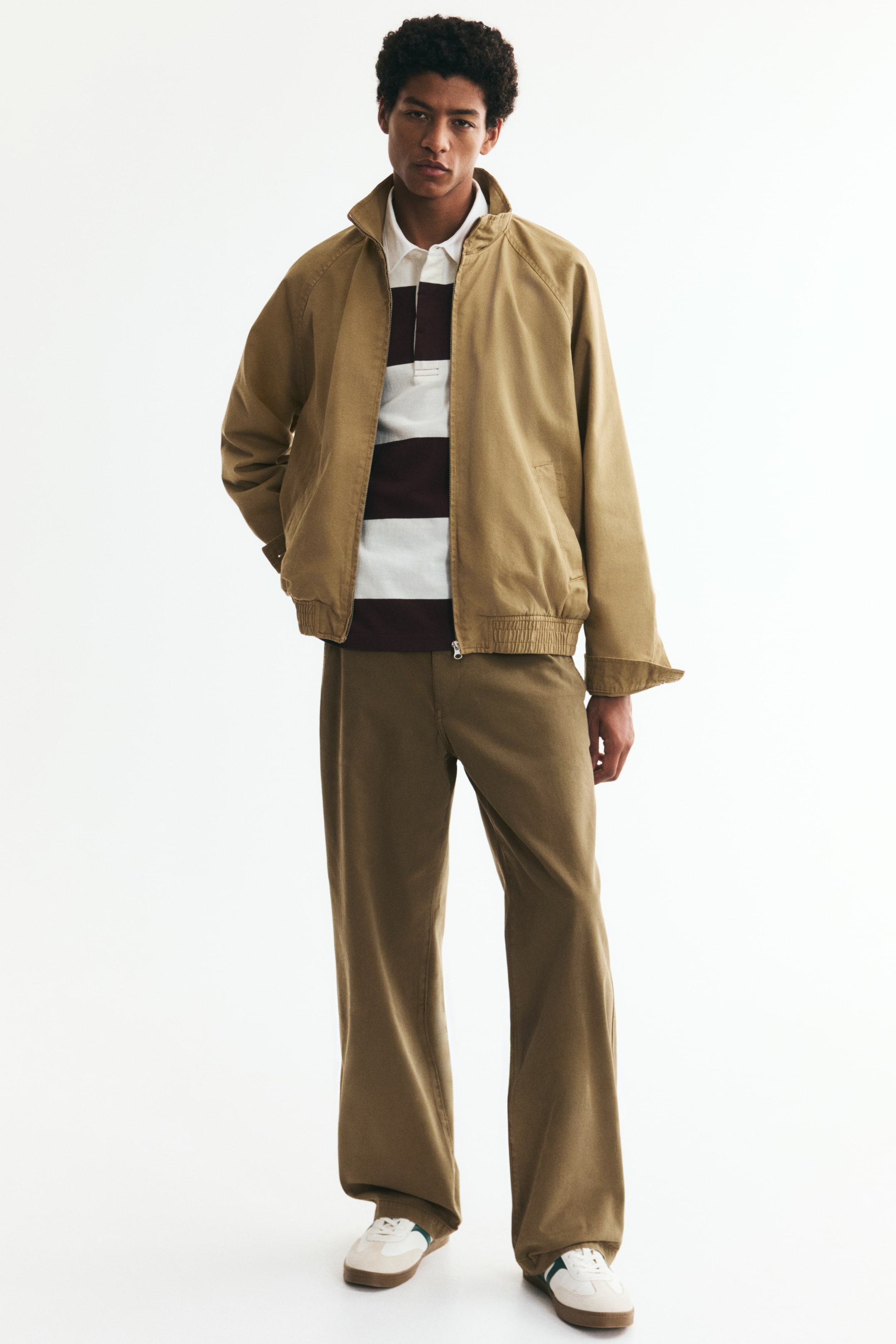 View larger image: Cotton twill chinos featuring a zip fly and button fastening, diagonal side pockets, straight legs, and a relaxed fit. The model is wearing the chinos, styled with a striped polo shirt, a light brown jacket, and trainers.