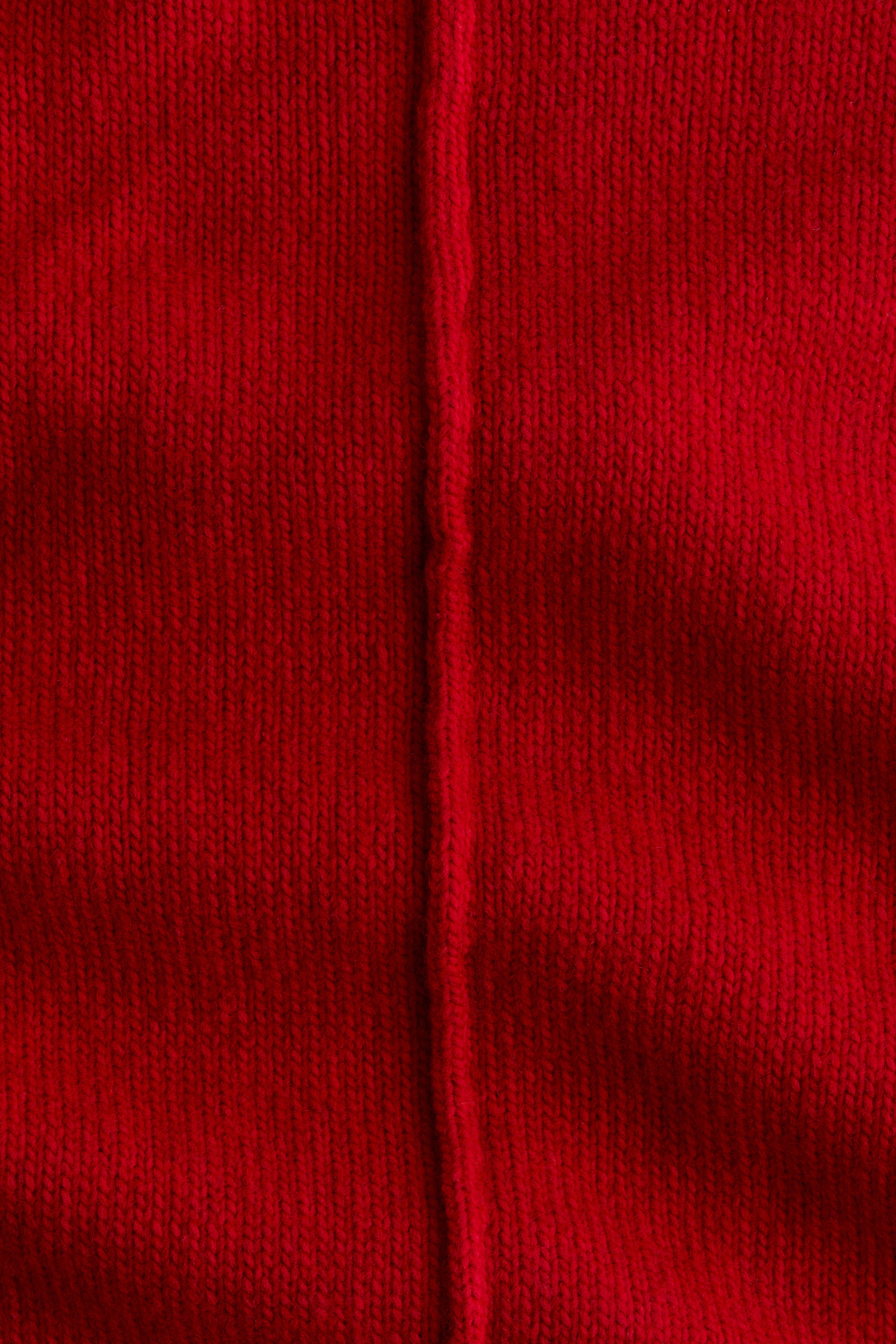 Büyük resmi görüntüle: Kareyi dolduran kırmızı bir örgü kumaş, düz örgü deseni ve ortasından geçen belirgin bir dikey dikişle sergileniyor.