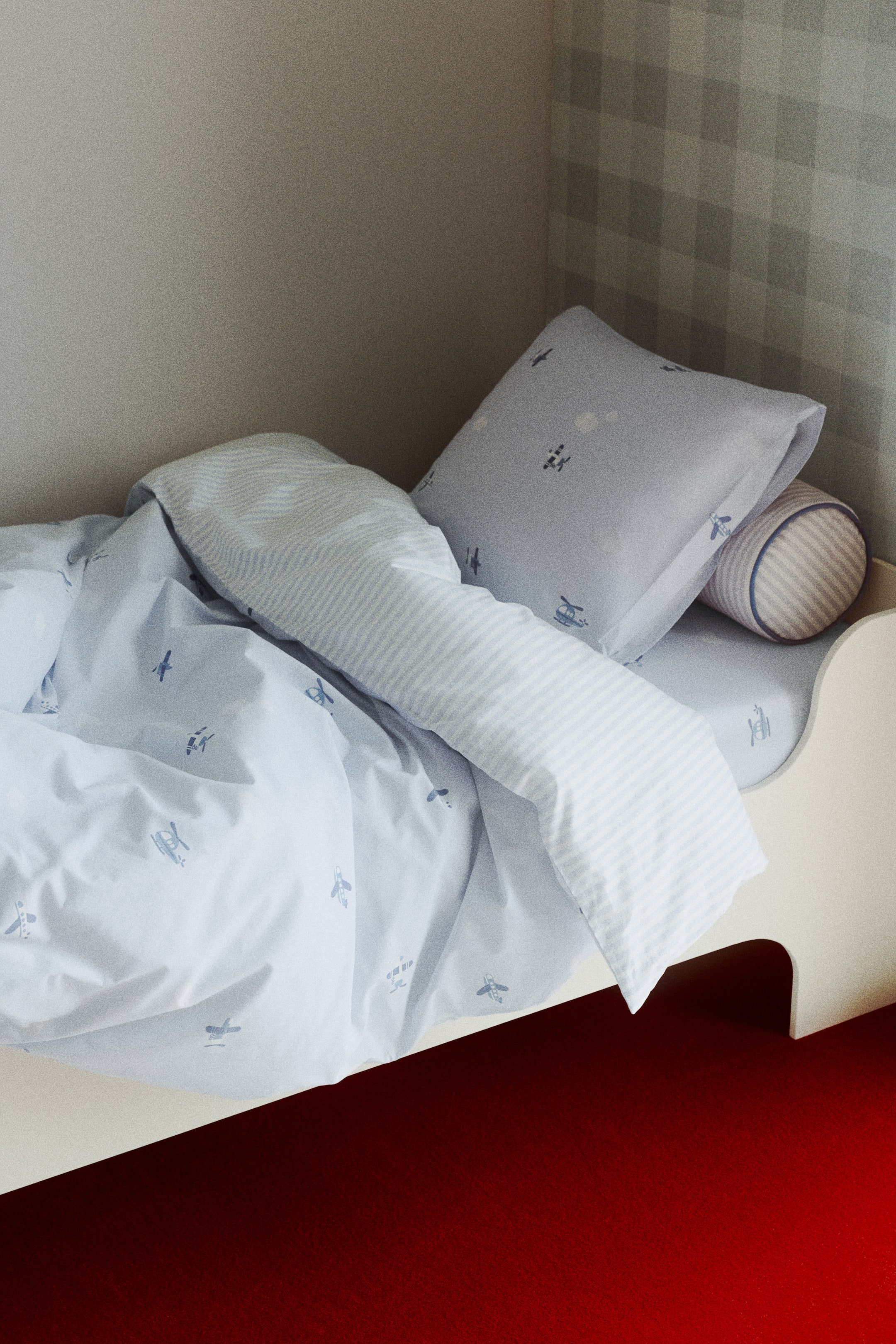 Visualizza immagine più grande: Un set copripiumino è esposto su un letto, mostrando un copripiumino azzurro con una stampa integrale di piccoli aerei ed elicotteri sul davanti. Il retro del copripiumino rivela un motivo a righe azzurre e bianche, e una federa abbinata azzurra con la stessa stampa di aerei ed elicotteri è appoggiata sul letto.