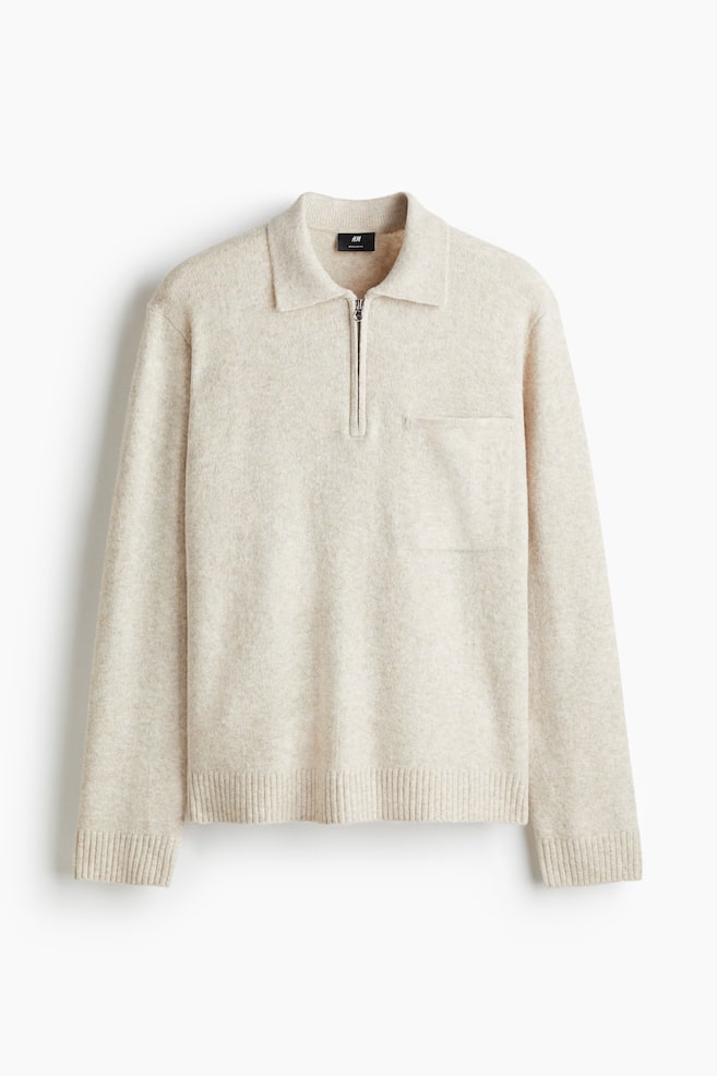 A light beige knit sweater is presented from the FRONT, featuring a polo collar, a half-zip closure with a silver-toned zipper, and a single patch pocket on the left chest. The sweater is finished with ribbed cuffs and a ribbed hem. - 1