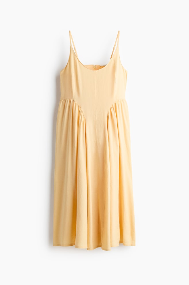 Un vestido de tirantes de color amarillo claro presenta un escote cuadrado con finos tirantes de espagueti, un corpiño ajustado y una falda midi acampanada con frunces en la cintura alta. Una cremallera parcial es visible en la parte superior de la espalda. - 1