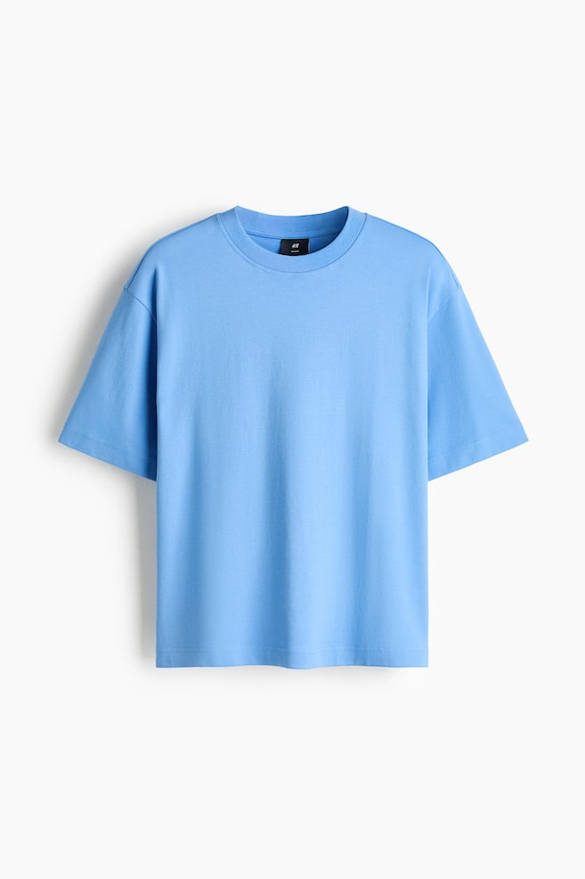 Een lichtblauw T-shirt van katoen interlock jersey wordt van voren getoond, met een relaxed fit, een ronde halslijn met ribboord en verlaagde schouders. Het kledingstuk hangt vlak, waardoor de rechte zoom en het nonchalante silhouet goed zichtbaar zijn. - 1