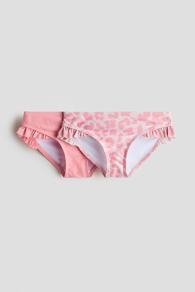 Fully lined bikini bottoms with a flounced trim at the sides are available in two variations. One is solid pink, while the other is light pink with a darker pink leopard print. Both are showcasing their front. - 1