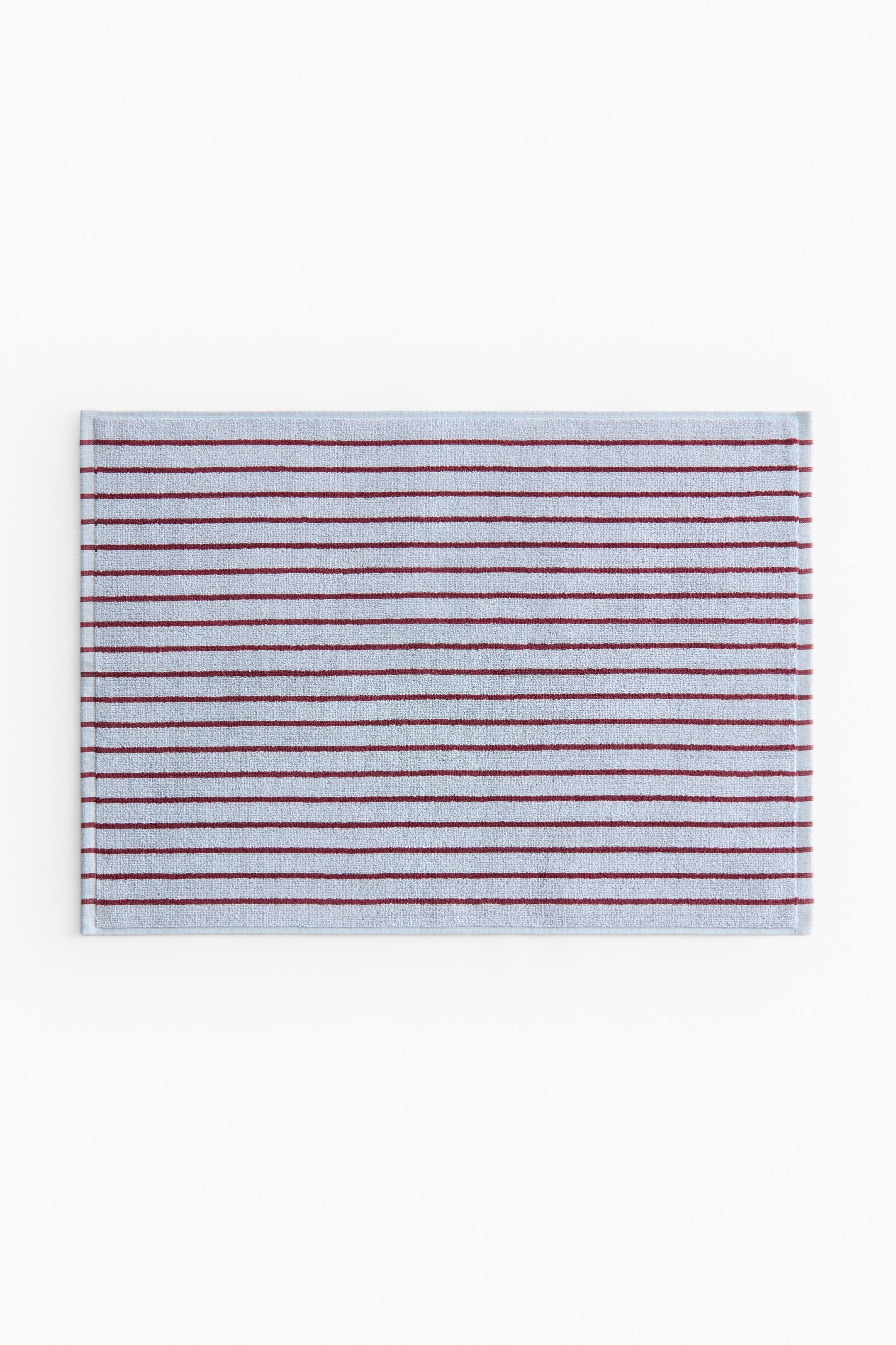 View larger image: A rectangular bath mat, viewed from the front, showcases a striped pattern. It features narrow horizontal dark red stripes against a light blue terry cloth surface, finished with a thin woven trim around its edges.